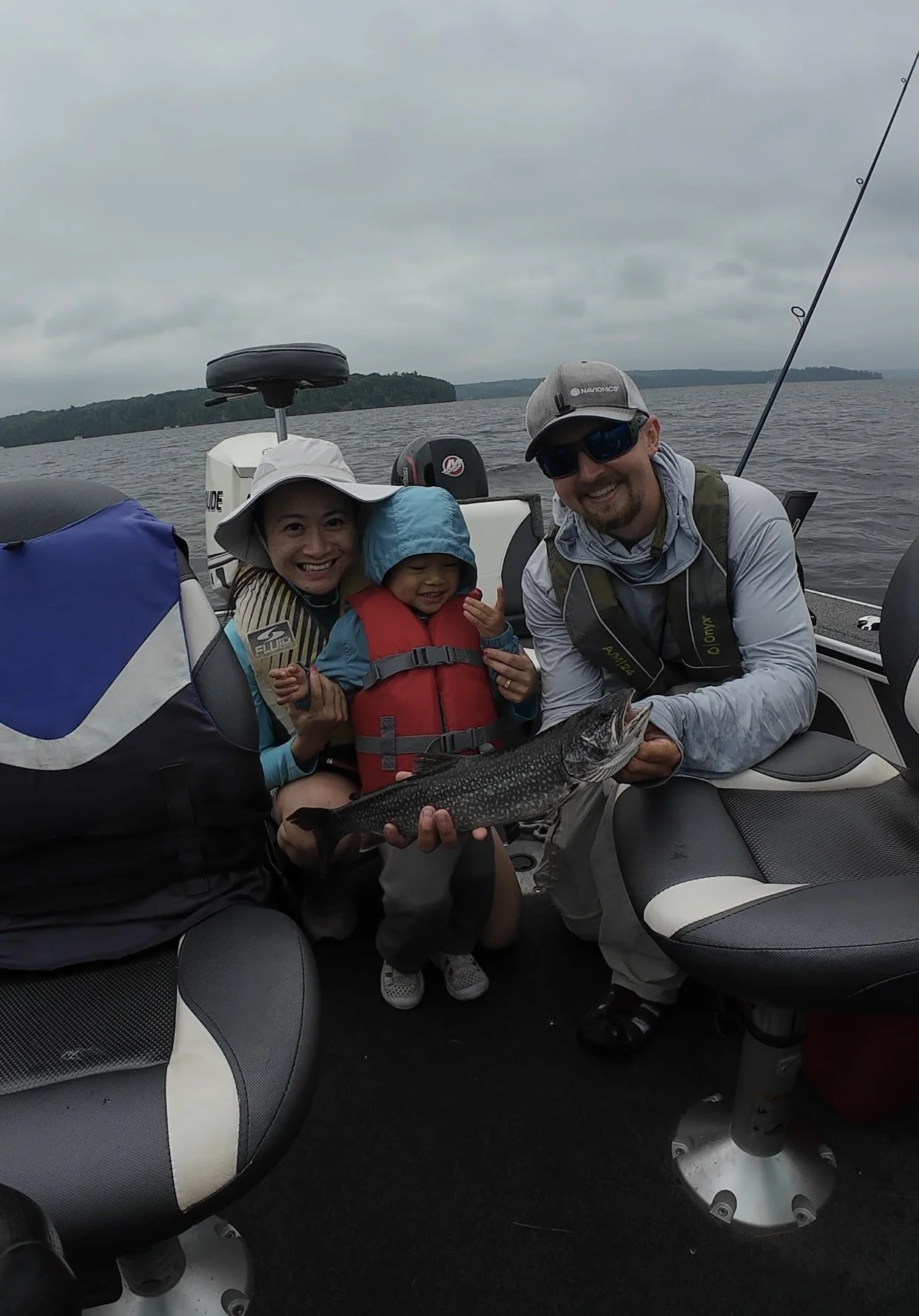 Family on a boat holding a fish, with water and cloudy sky in the background.