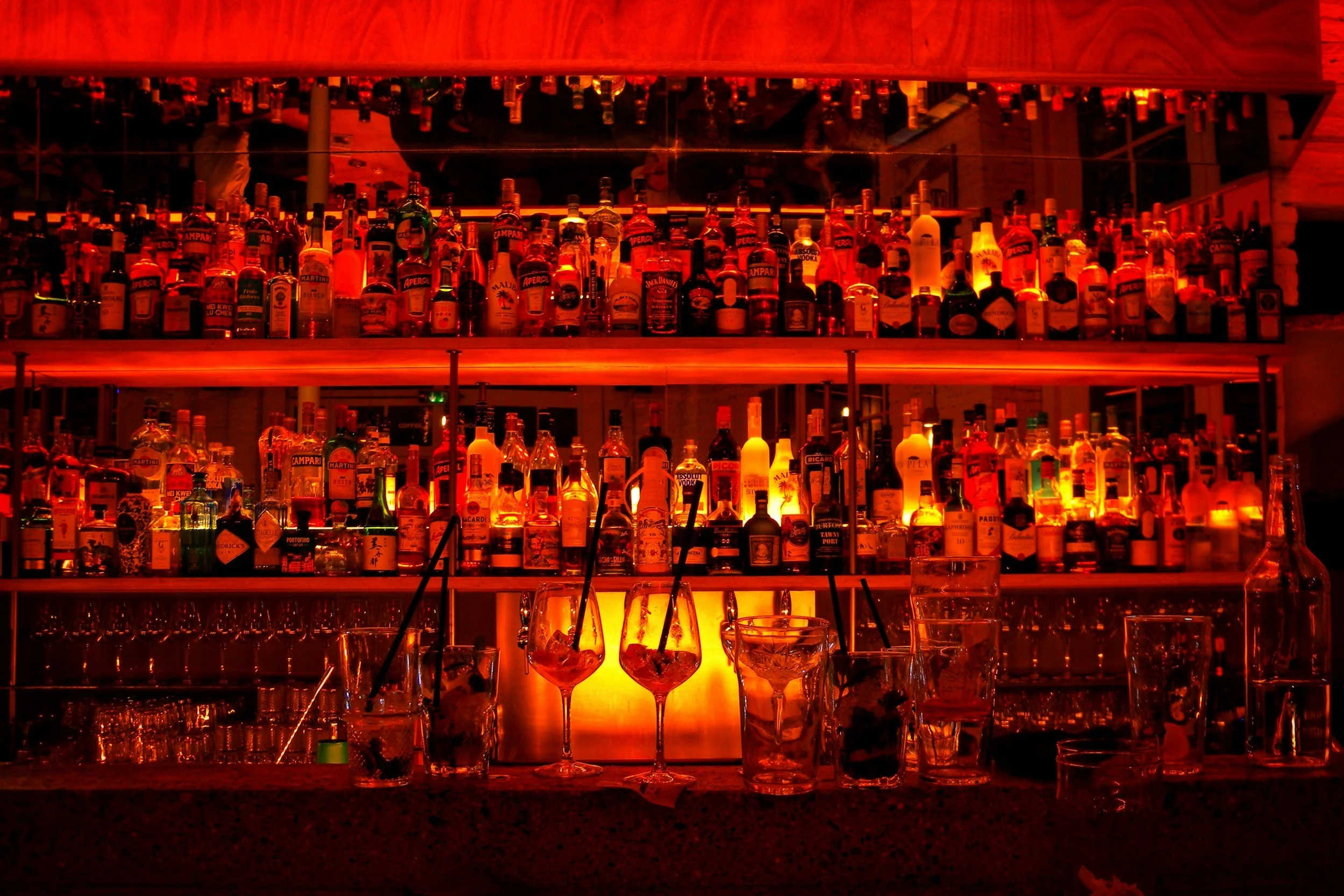 A bar shelf illuminated with red lighting, stocked with various bottles of liquor.