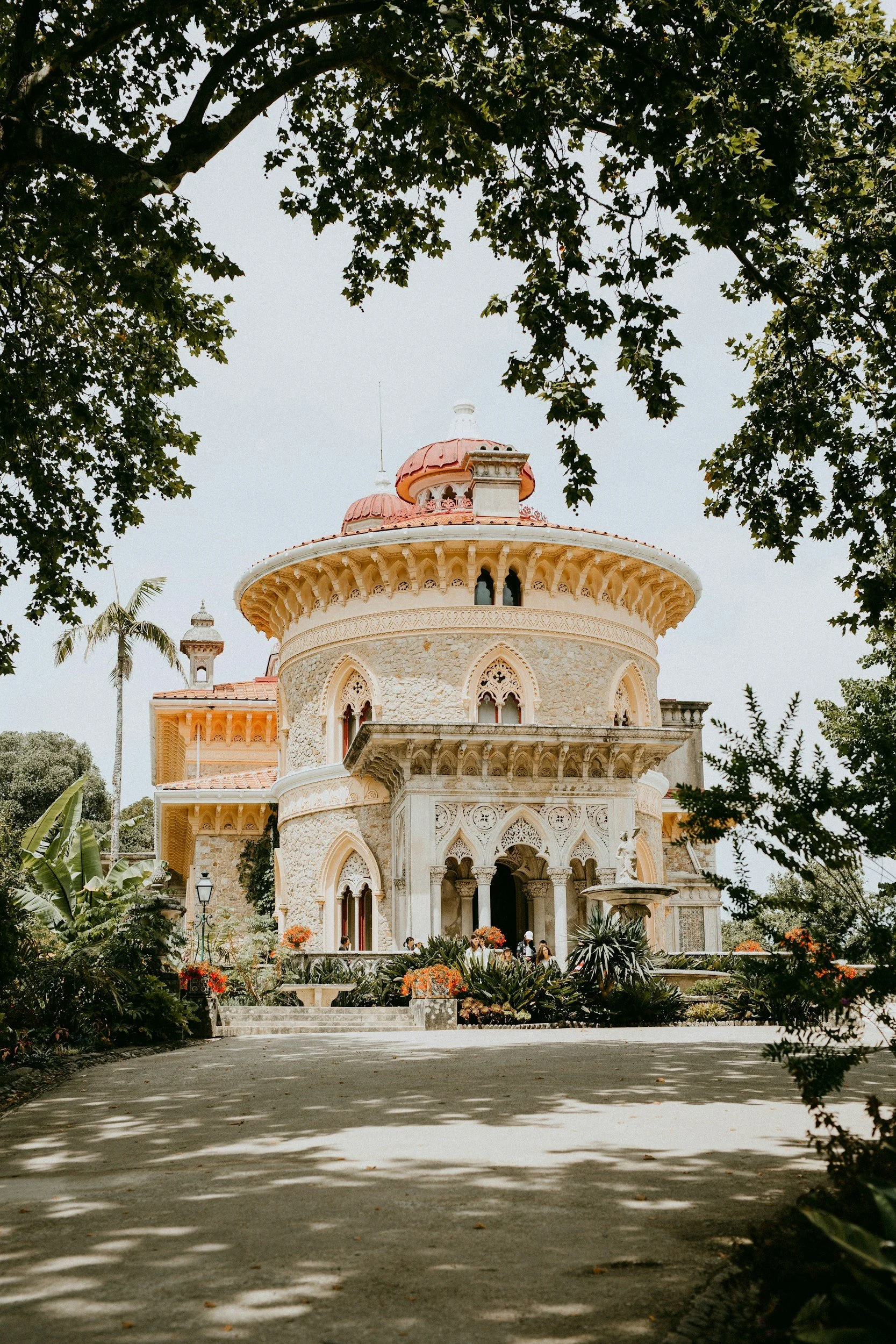 The historic Monserrate Palace in Sintra, Portugal, with ornate architectural details, surrounded by lush trees and plants, with a pathway leading up to the entrance.