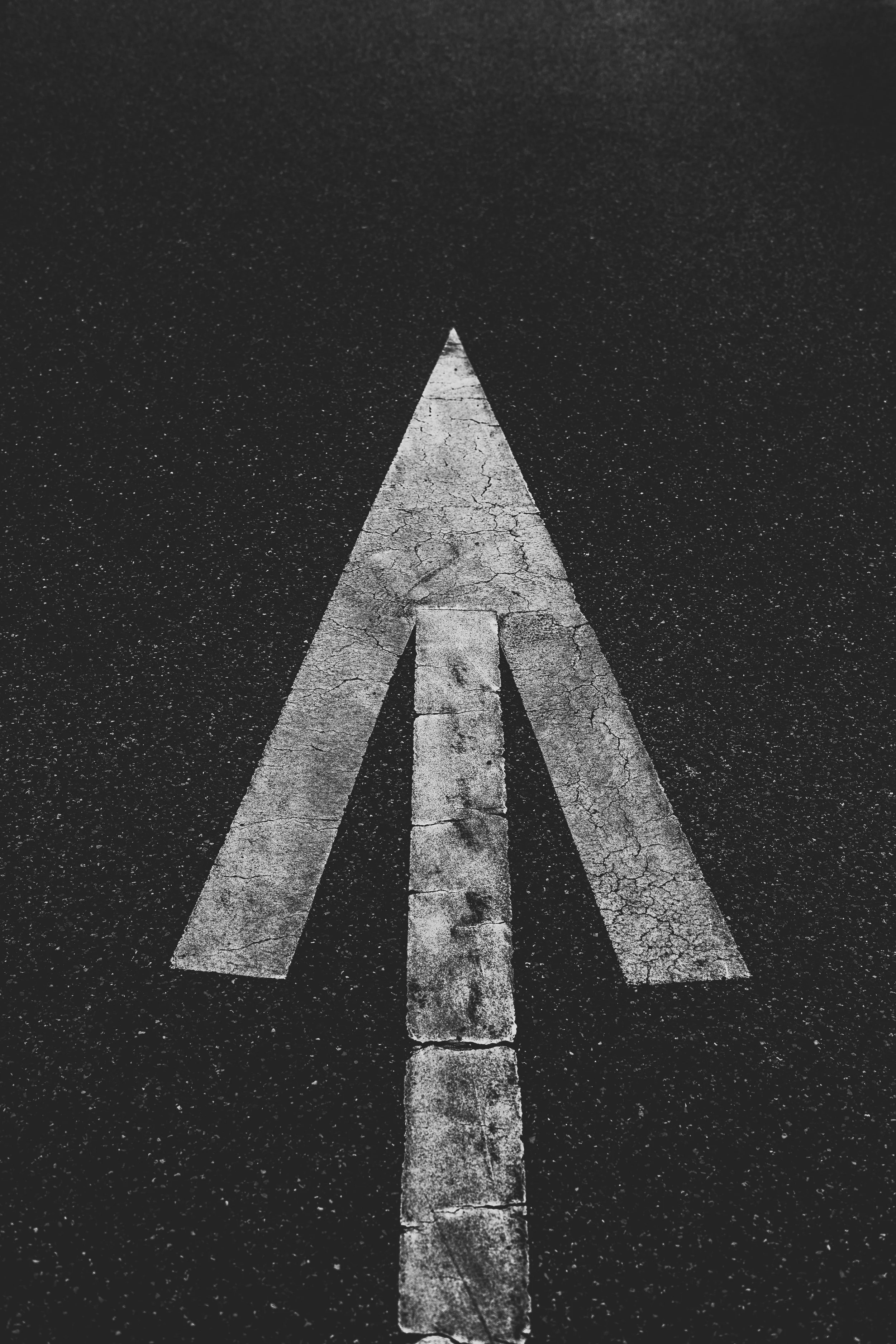 A close-up view of a worn street arrow painted on asphalt, pointing forward, in black and white.