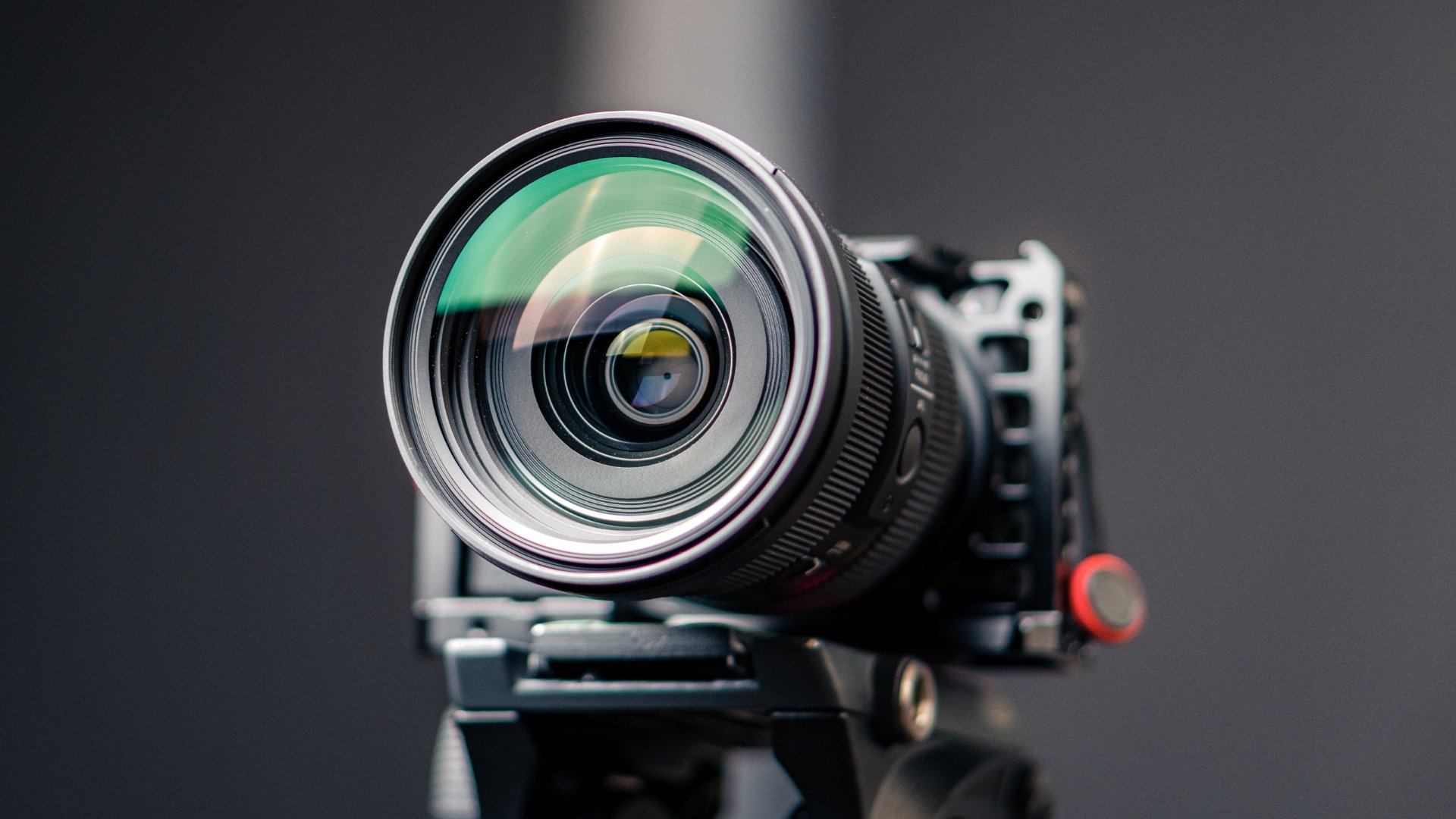 Close-up of a professional camera lens mounted on a camera body, set against a dark background.