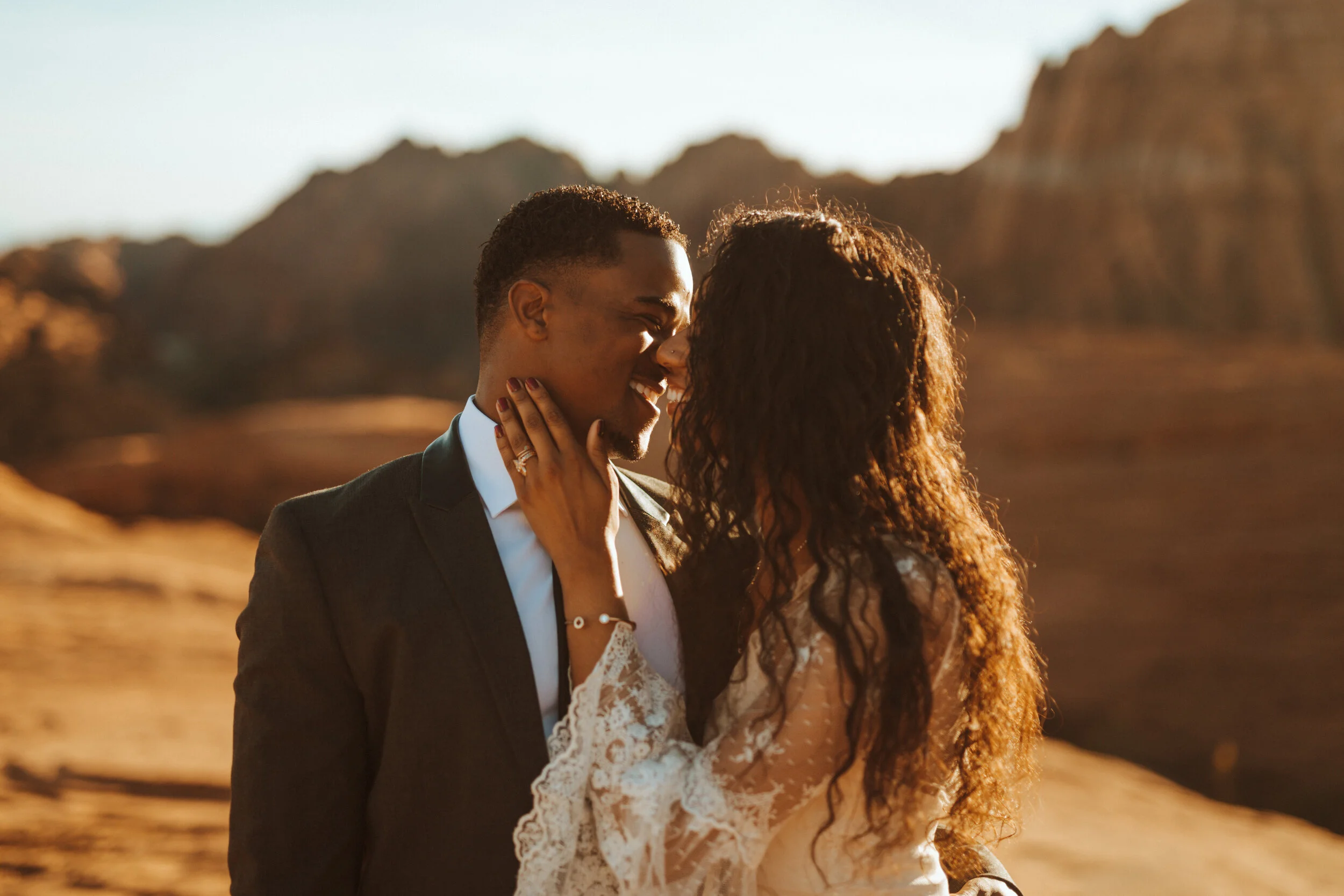 A couple sharing an intimate moment outdoors at sunset, with mountains in the background.