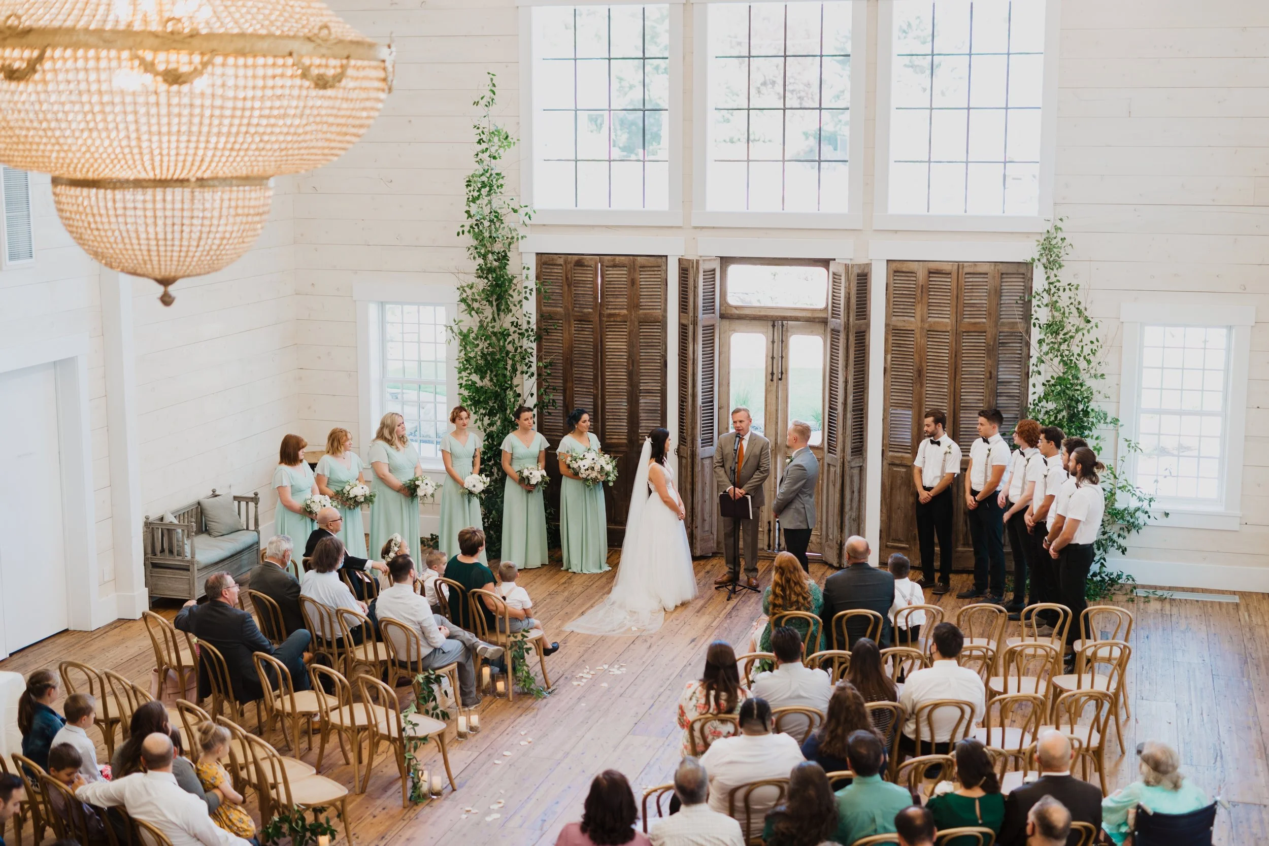 Bride and groom standing together during an indoor Utah wedding ceremony with their wedding party and guests surrounding them.