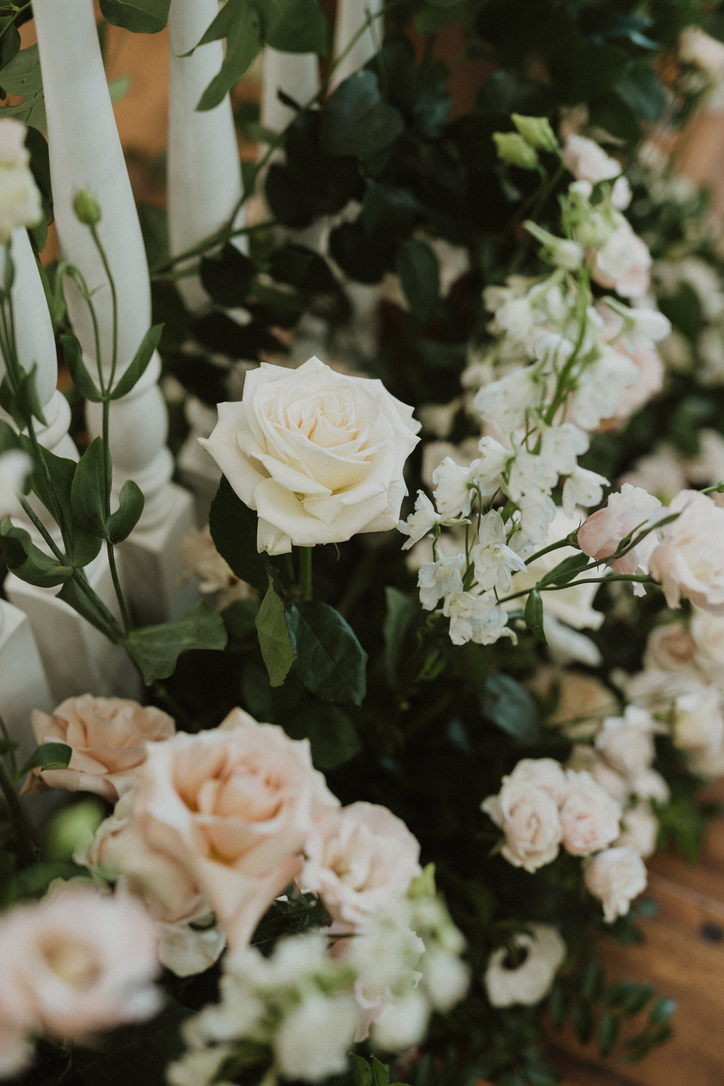 Various flowers, including white and light pink roses and white small blossoms, with green leaves, arranged in a floral display.