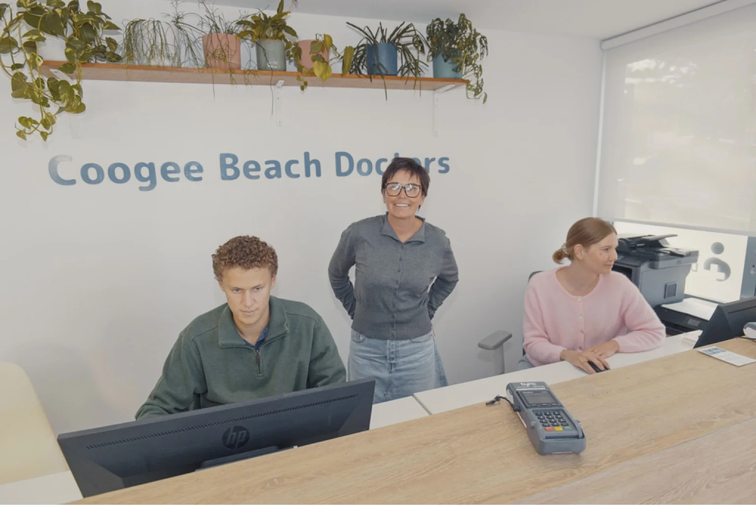 The reception team at Coogee Beach Doctors with the practice signage on the wall behind.
