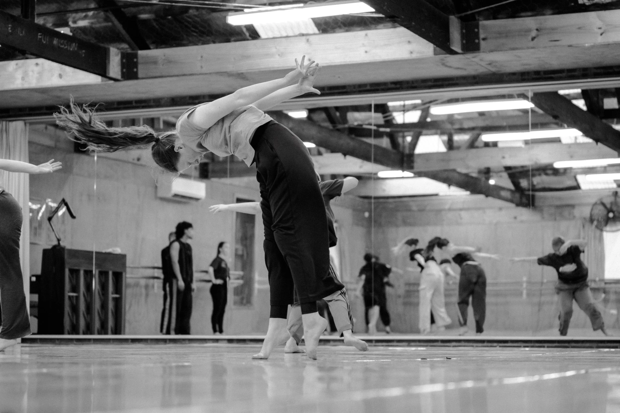 A dancer with their head forward iand arms reaching back while on demi pointe with parallel feet one leg in front of the other