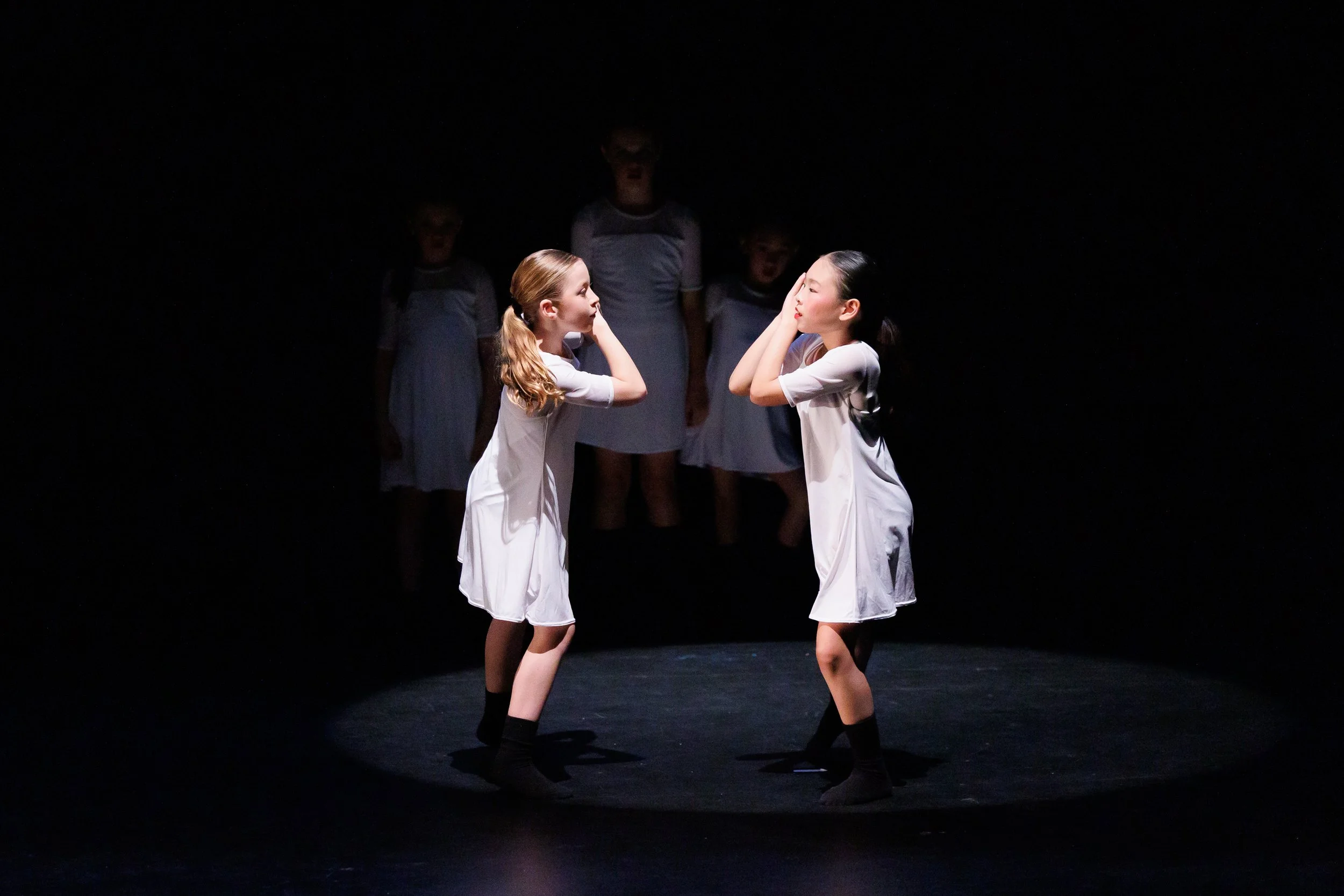 Erin and Olivia perform Blasen. Dancing in white dresses and black crew socks they look to one another with hands by face and reaching out their upstage foot