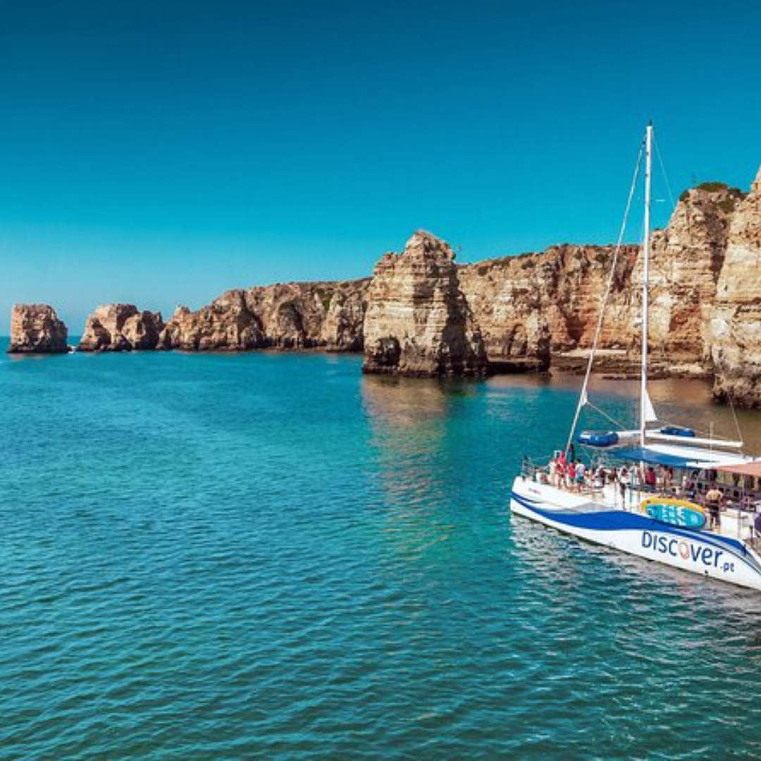 Catamaran sailing near steep coastal cliffs in clear blue water