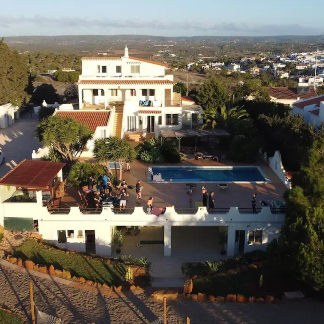 Large white villa with a pool and terrace, surrounded by trees and overlooking a town and countryside.