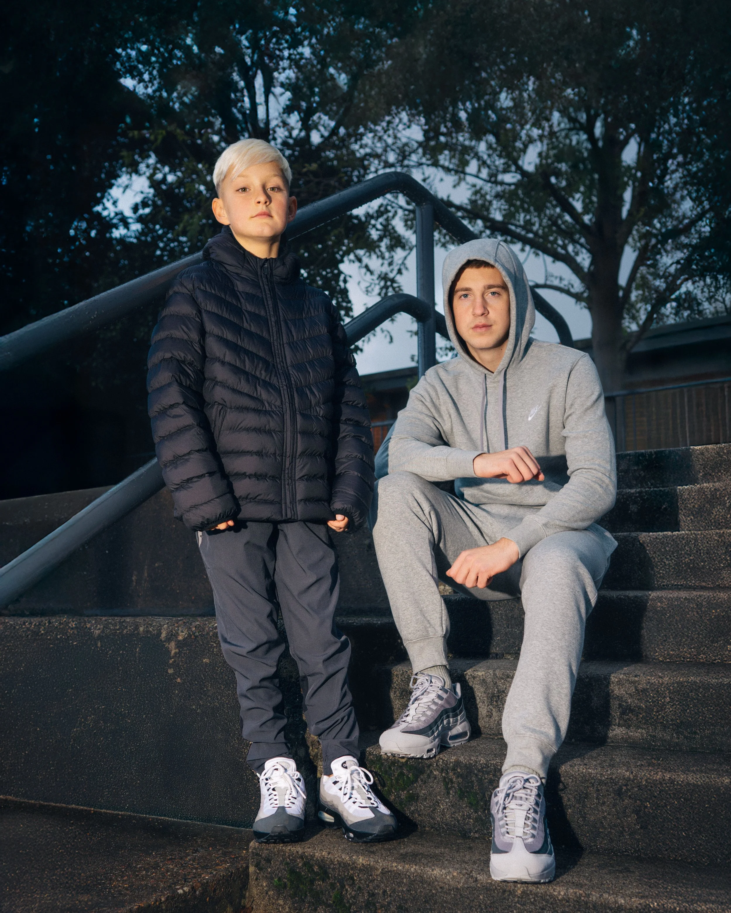Two boys in athleticwear studying outdoors on a dusk or evening day, with trees and stairs in the background.