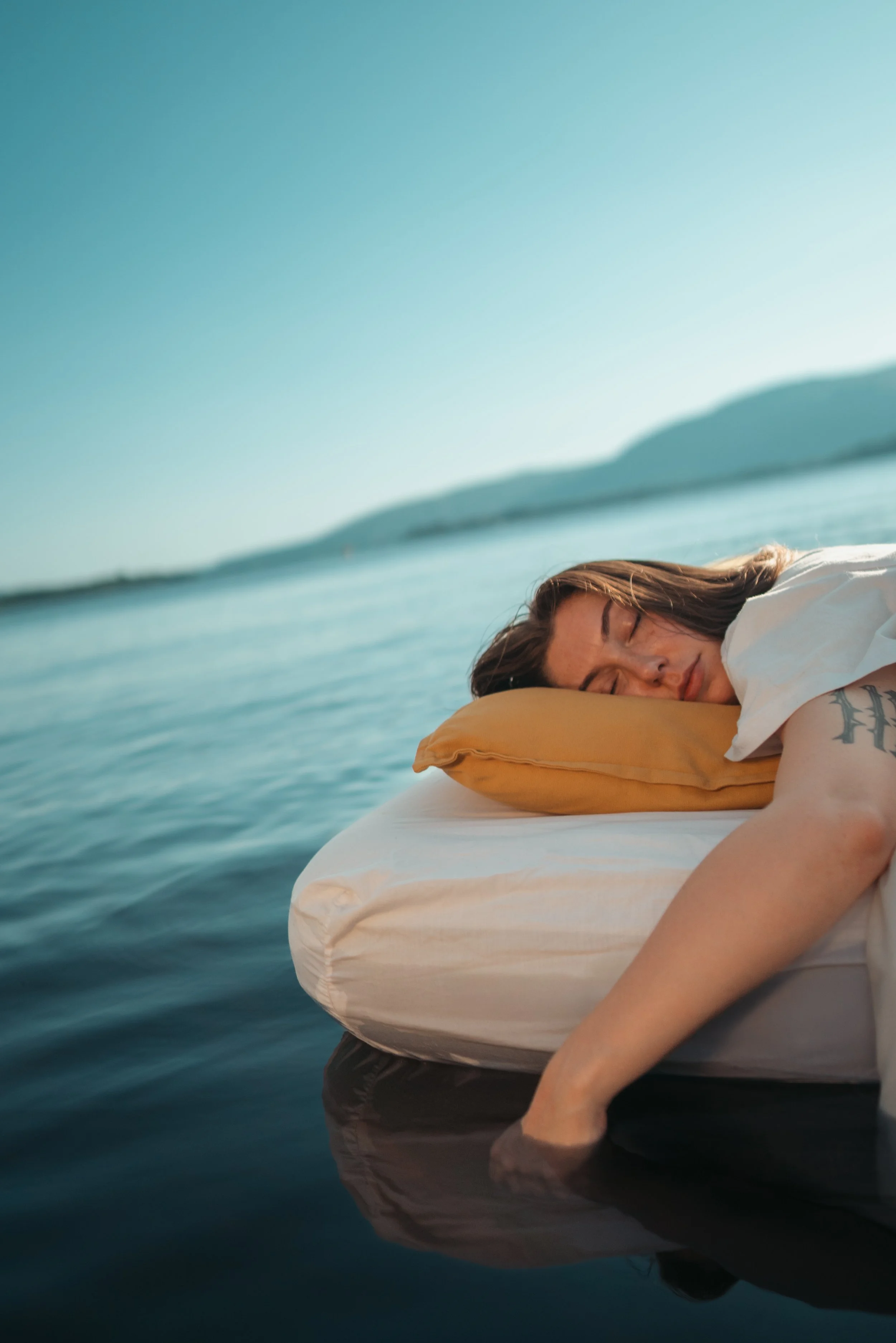 Woman sleeping on an inflatable mattress in a body of water with mountains in the background.