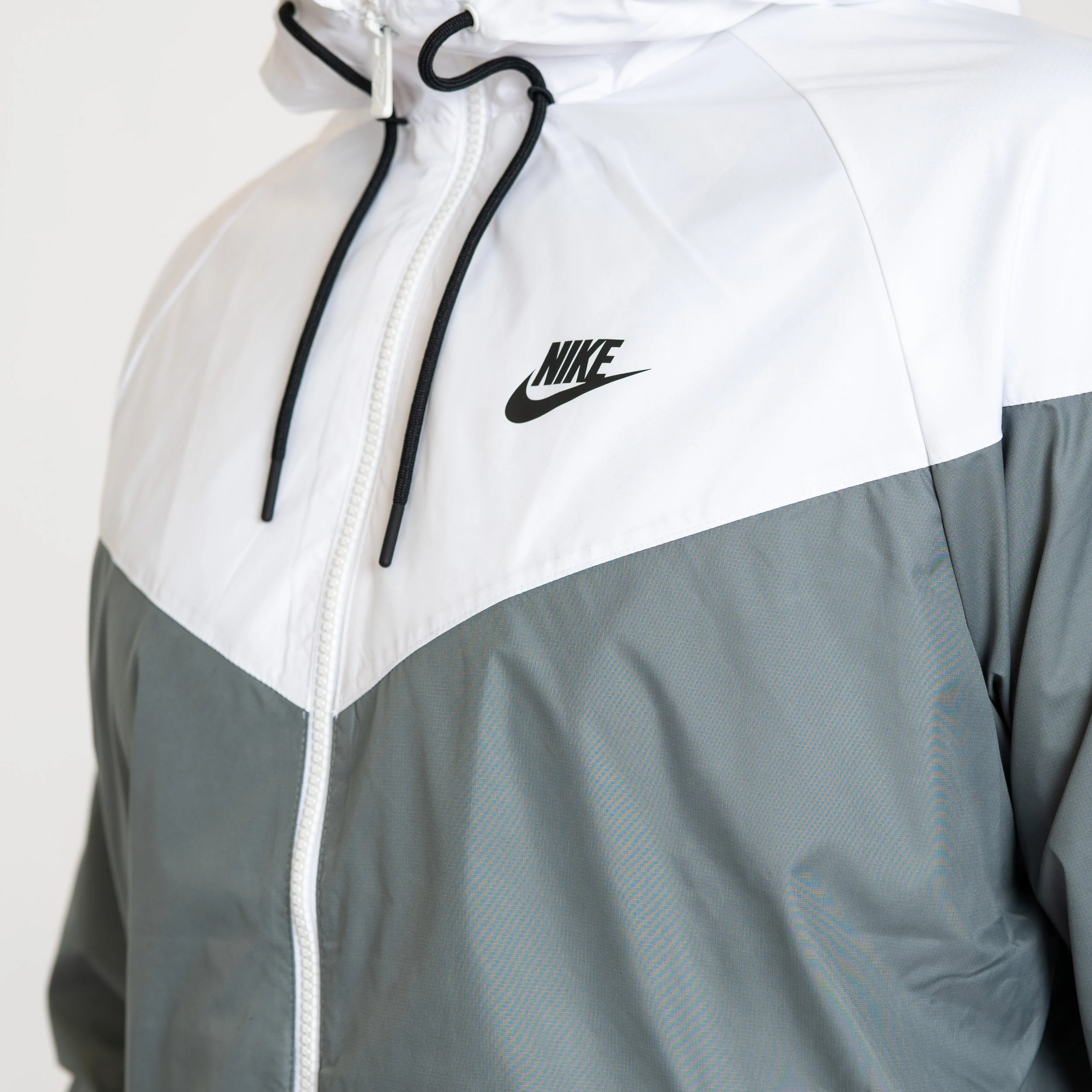 Close-up of a Nike windbreaker jacket with a white upper section and gray lower section, featuring the Nike logo in black on the chest.
