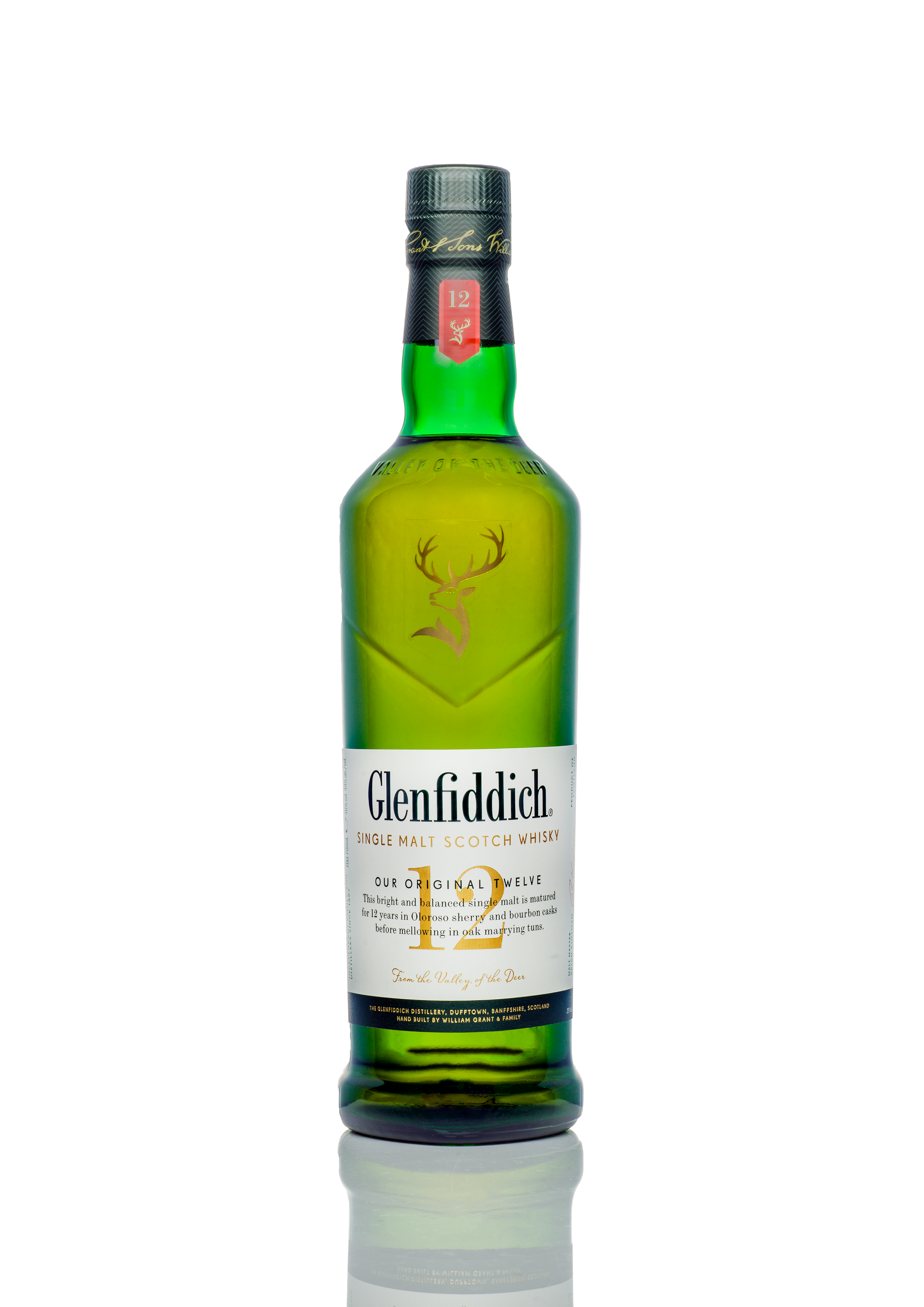 Green bottle of Glenfiddich single malt scotch whisky with white label and gold accents, standing upright on a reflective surface.