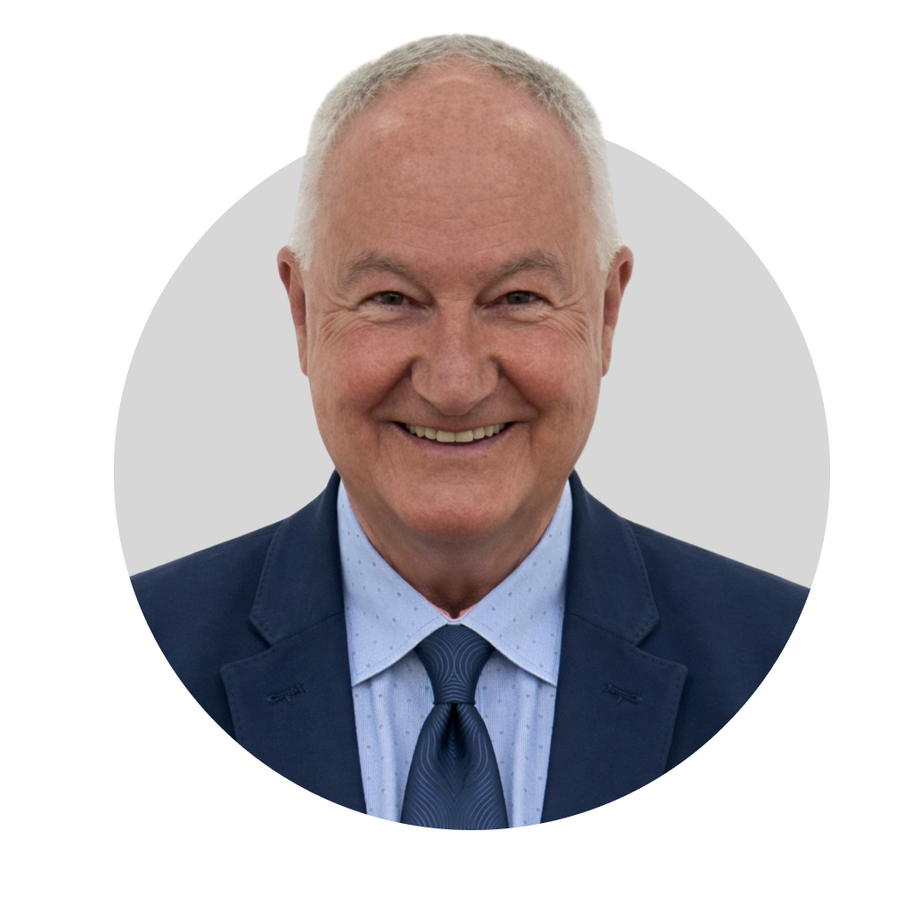 Smiling older man with short gray hair, wearing a navy suit, light blue dress shirt, and navy tie, against a light gray background.