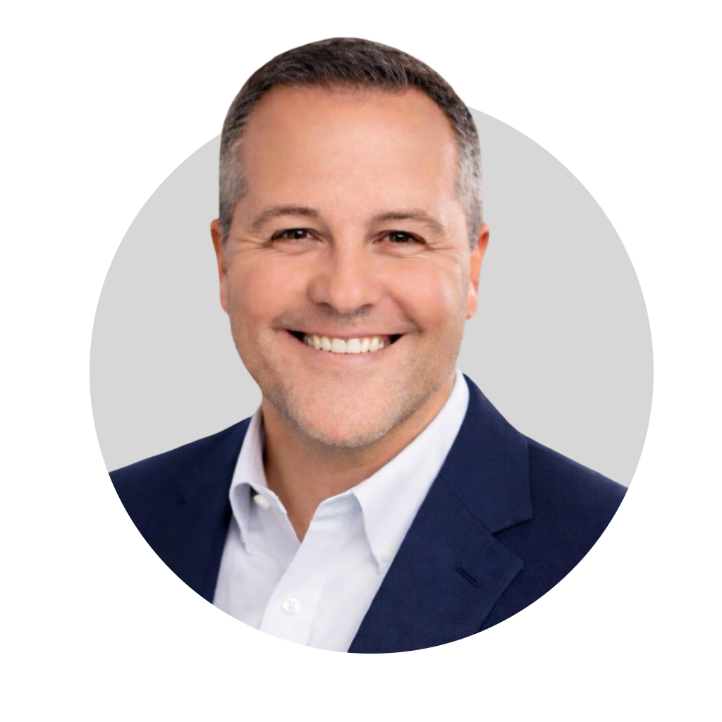 Headshot of a smiling man with short gray hair, wearing a white collared shirt and dark blazer, against a light gray background.