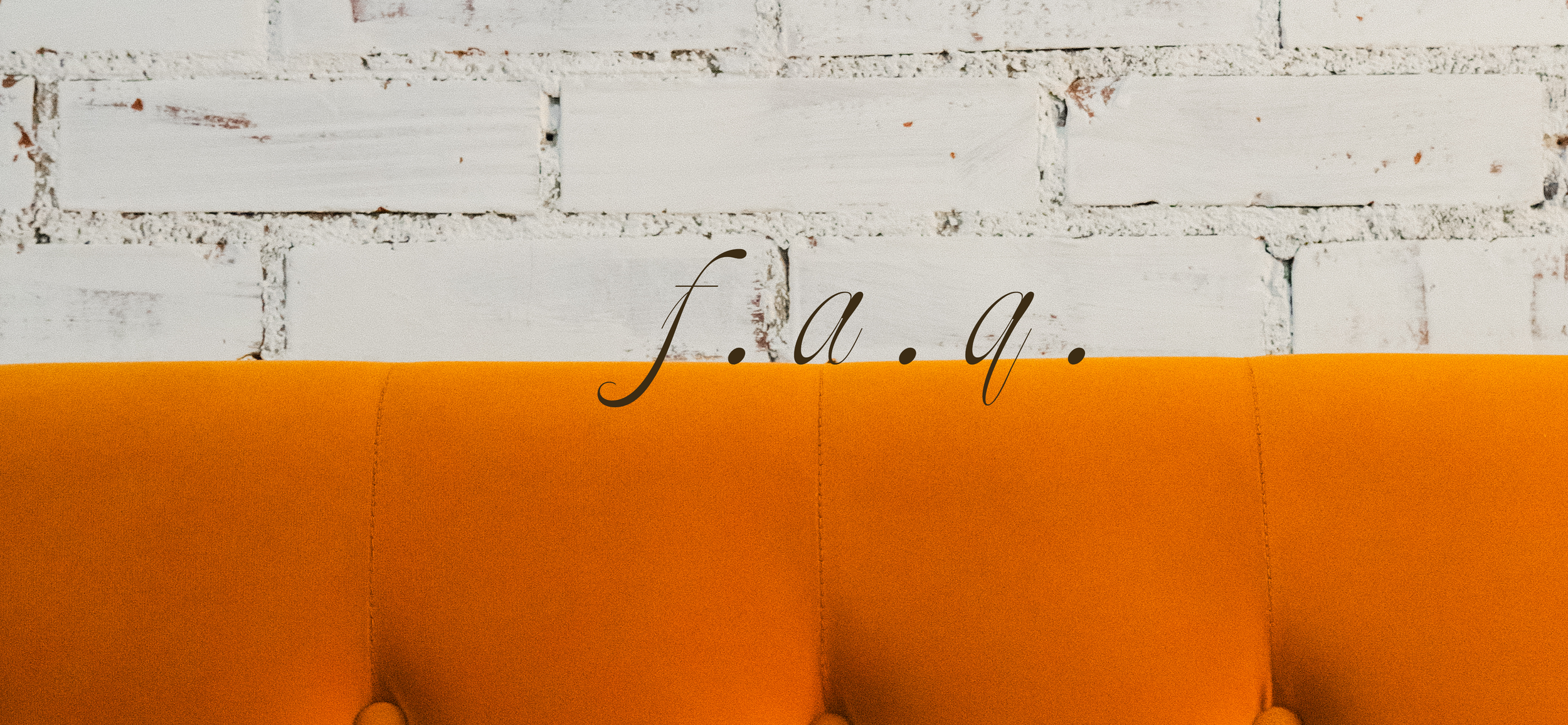 Decorative sign with the word "J.A.Q." in black cursive font on an orange cushioned surface against a white brick wall background.