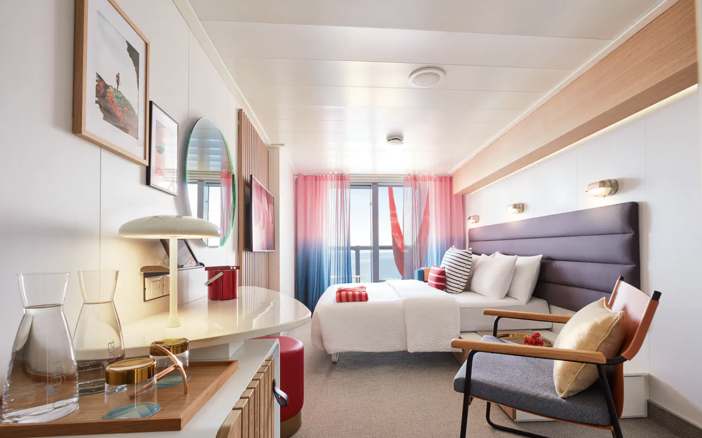 Modern hotel room with twin beds, desk, chair, colorful curtains, wall art, and ocean view.