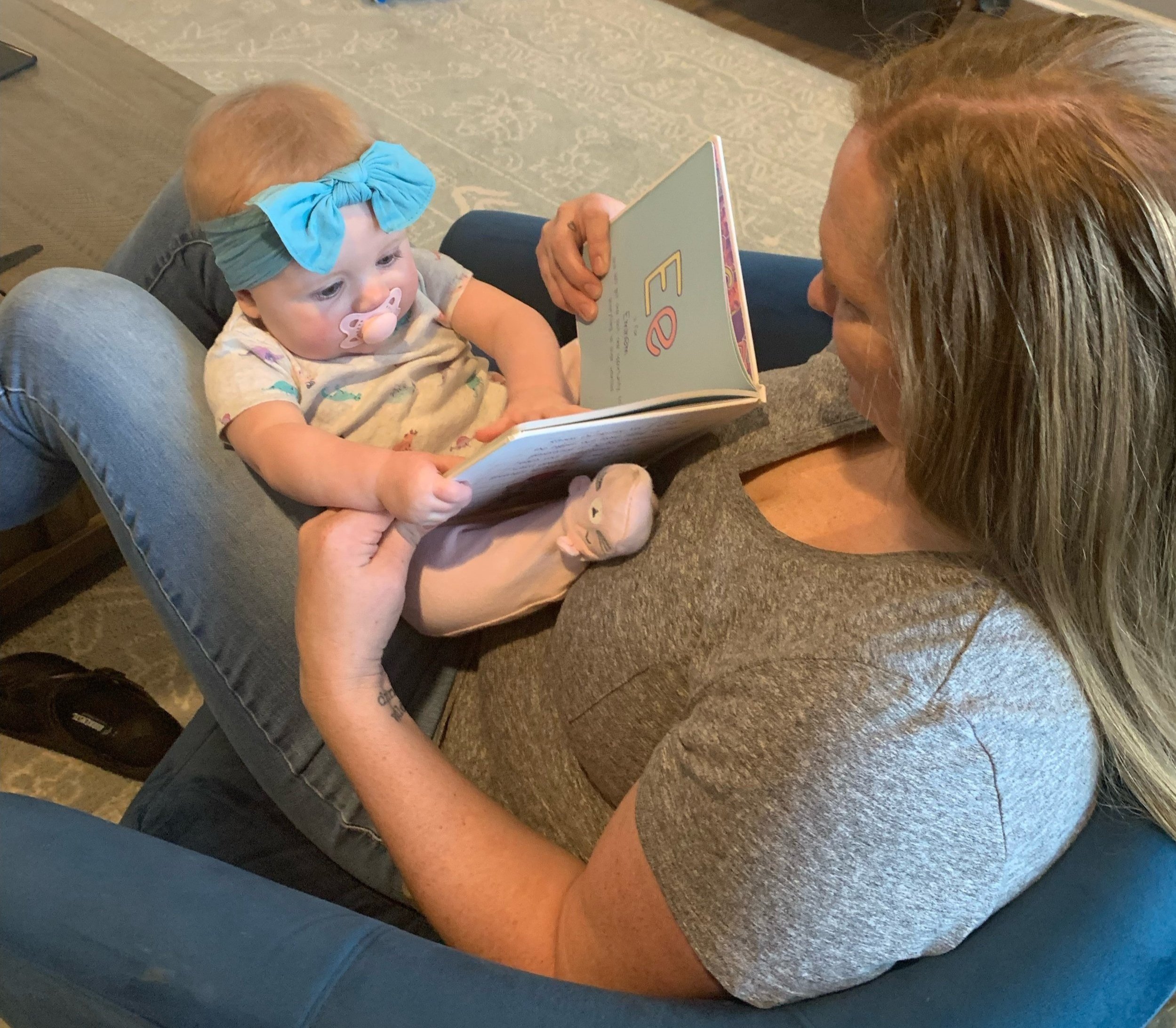 white female reading to baby with blue bow sitting on her knees