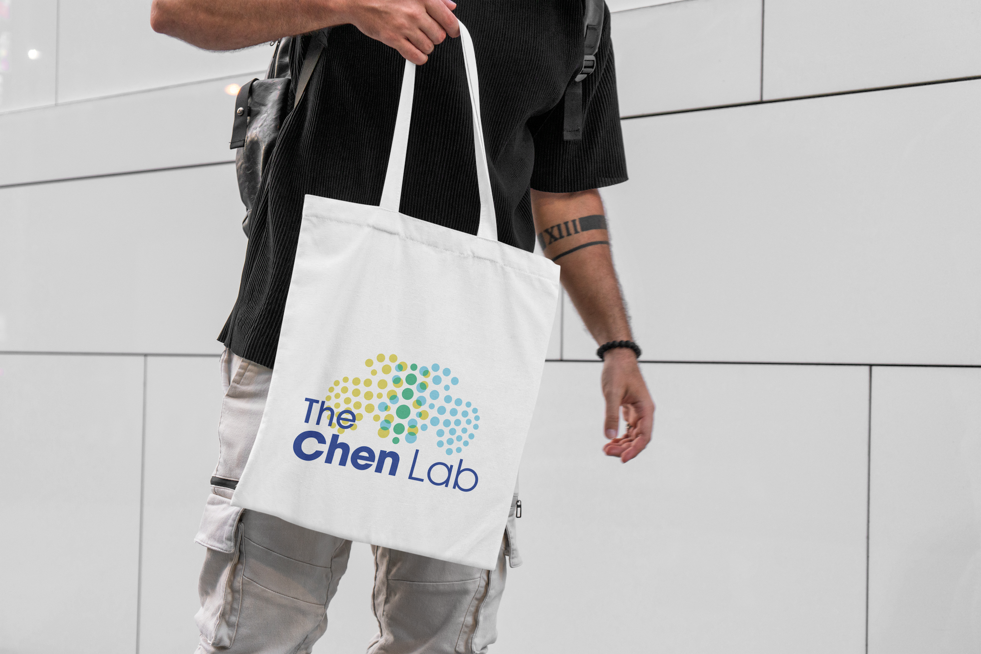 Mockup of a man holding a white tote bag displaying custom lab logo for the Chen Lab