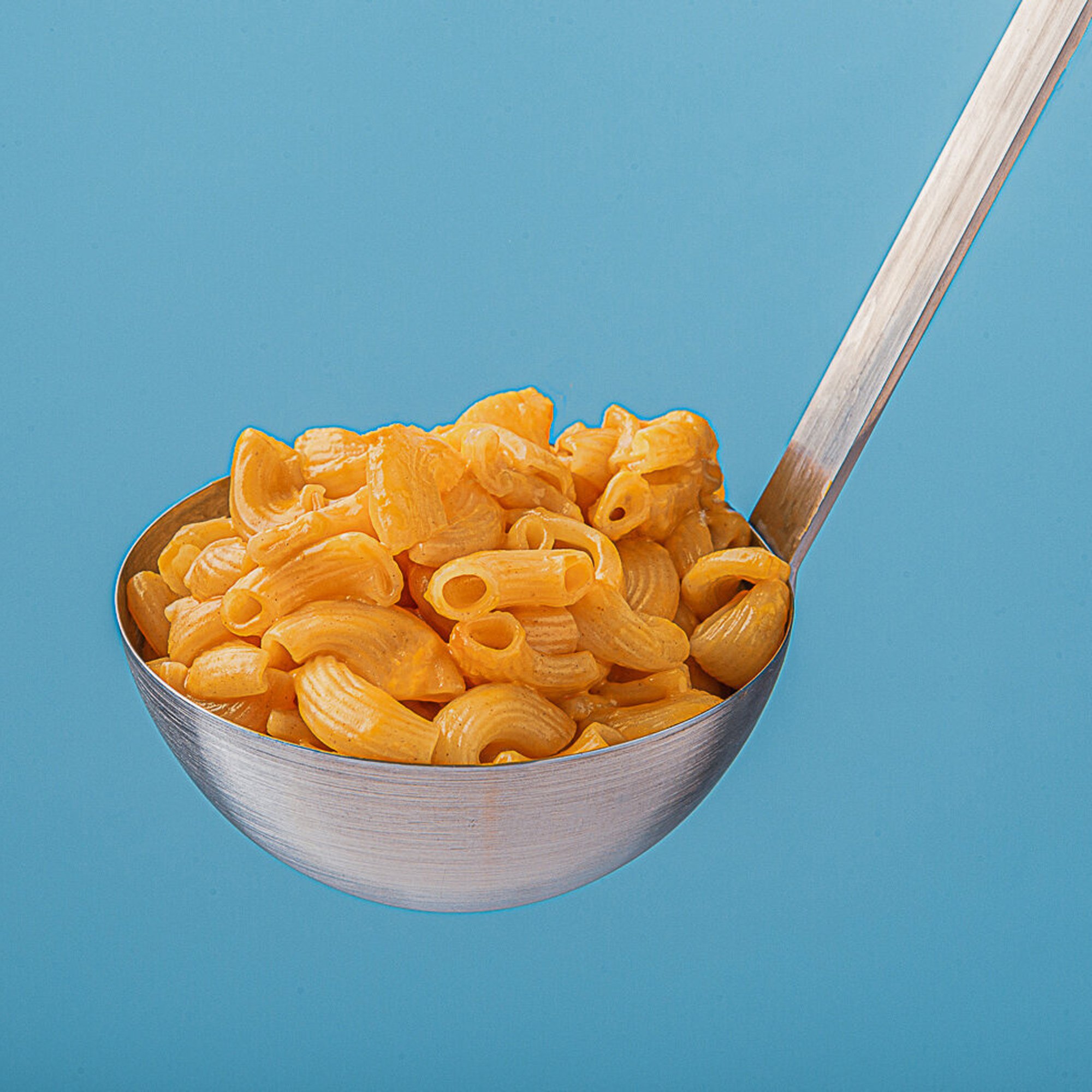  Food photography, a ladle full of mac and cheese photographed against a contrasting blue background 