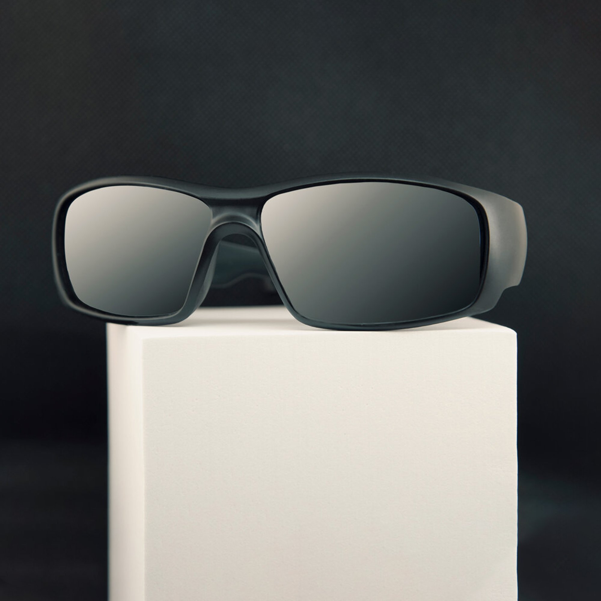  Black sunglasses photographed on a white block against a black background. 
