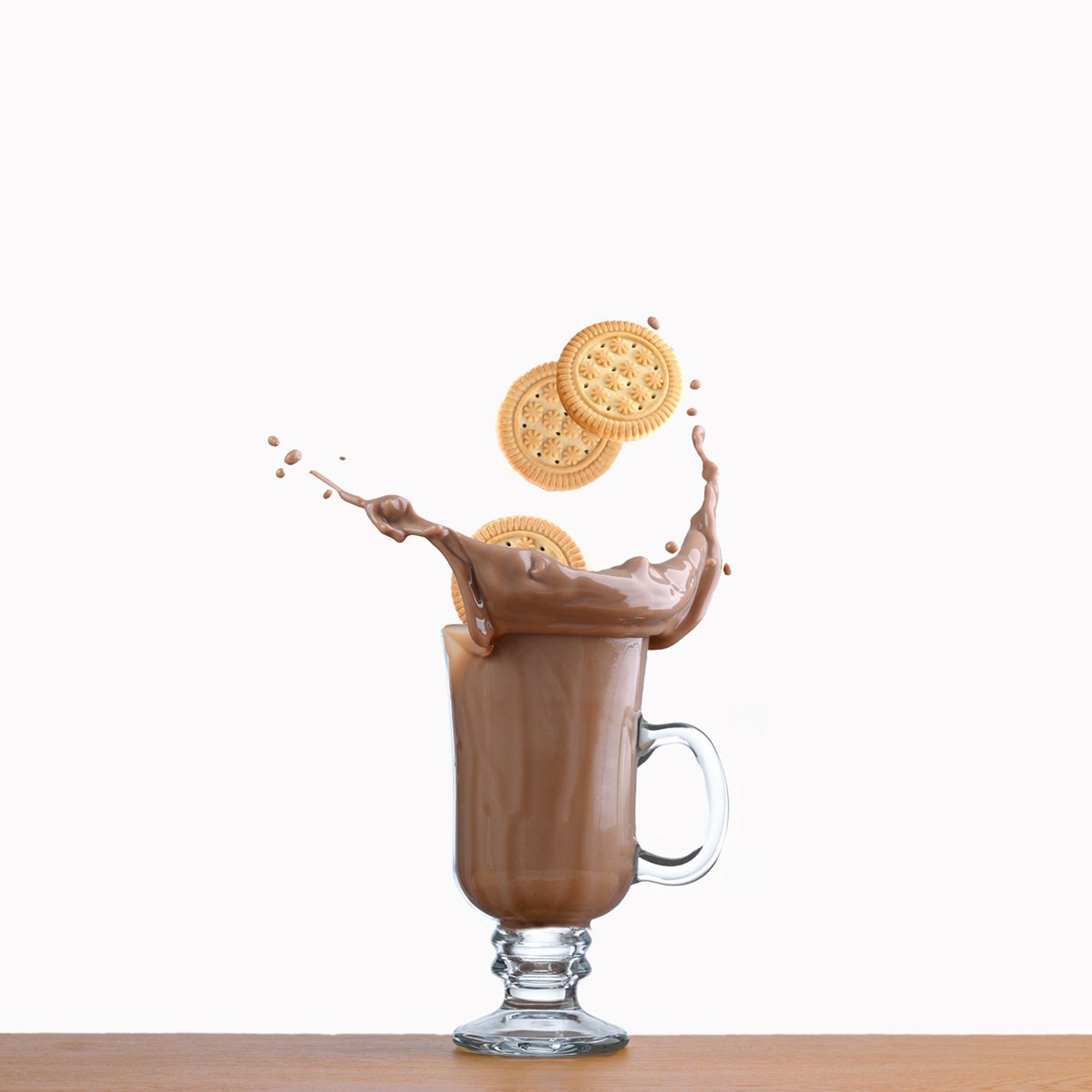  Sandwich cookies are splashed into a glass of chocolate milk against a white background. 