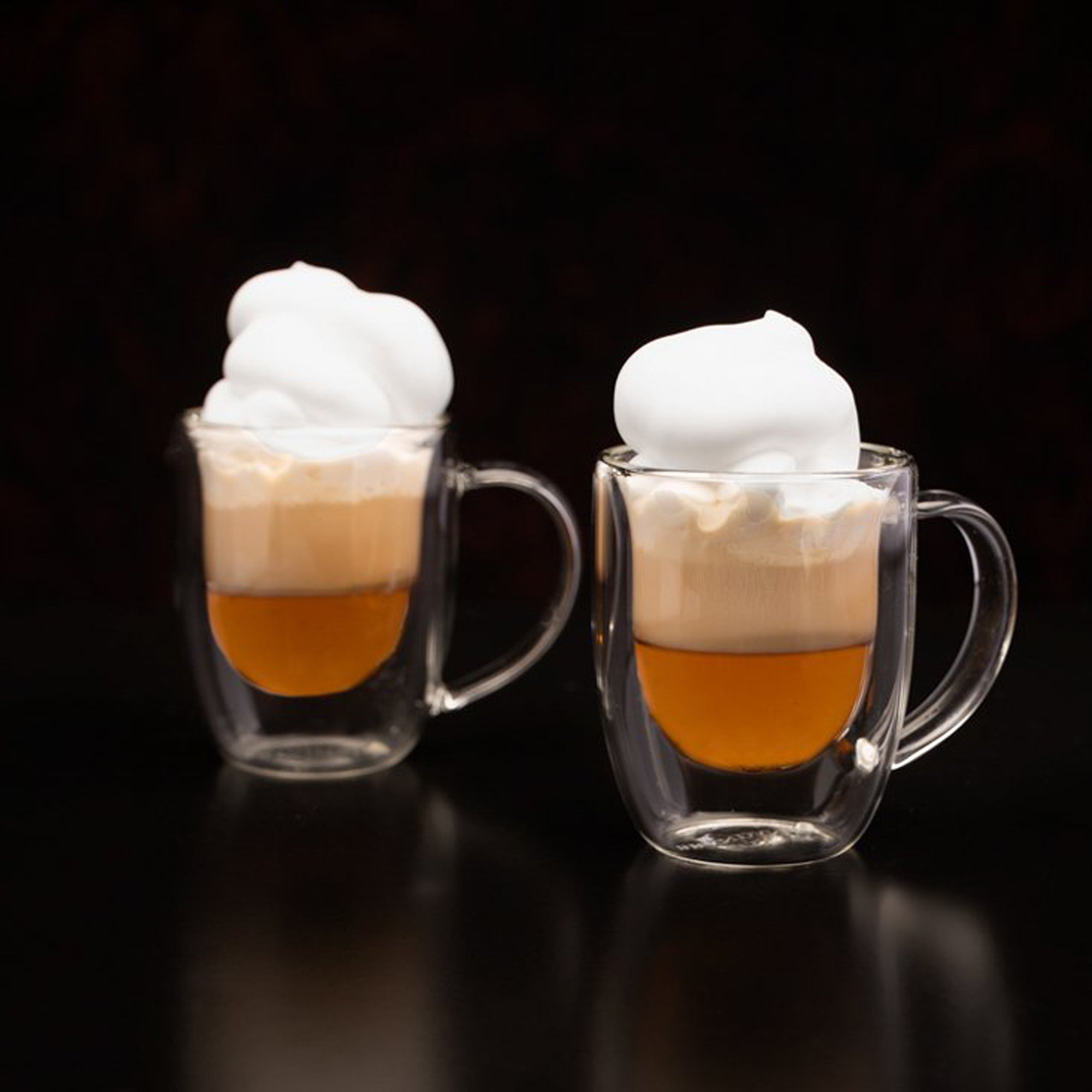  two small cups of fancy coffee with whipped cream photographed on a black table with a black background 