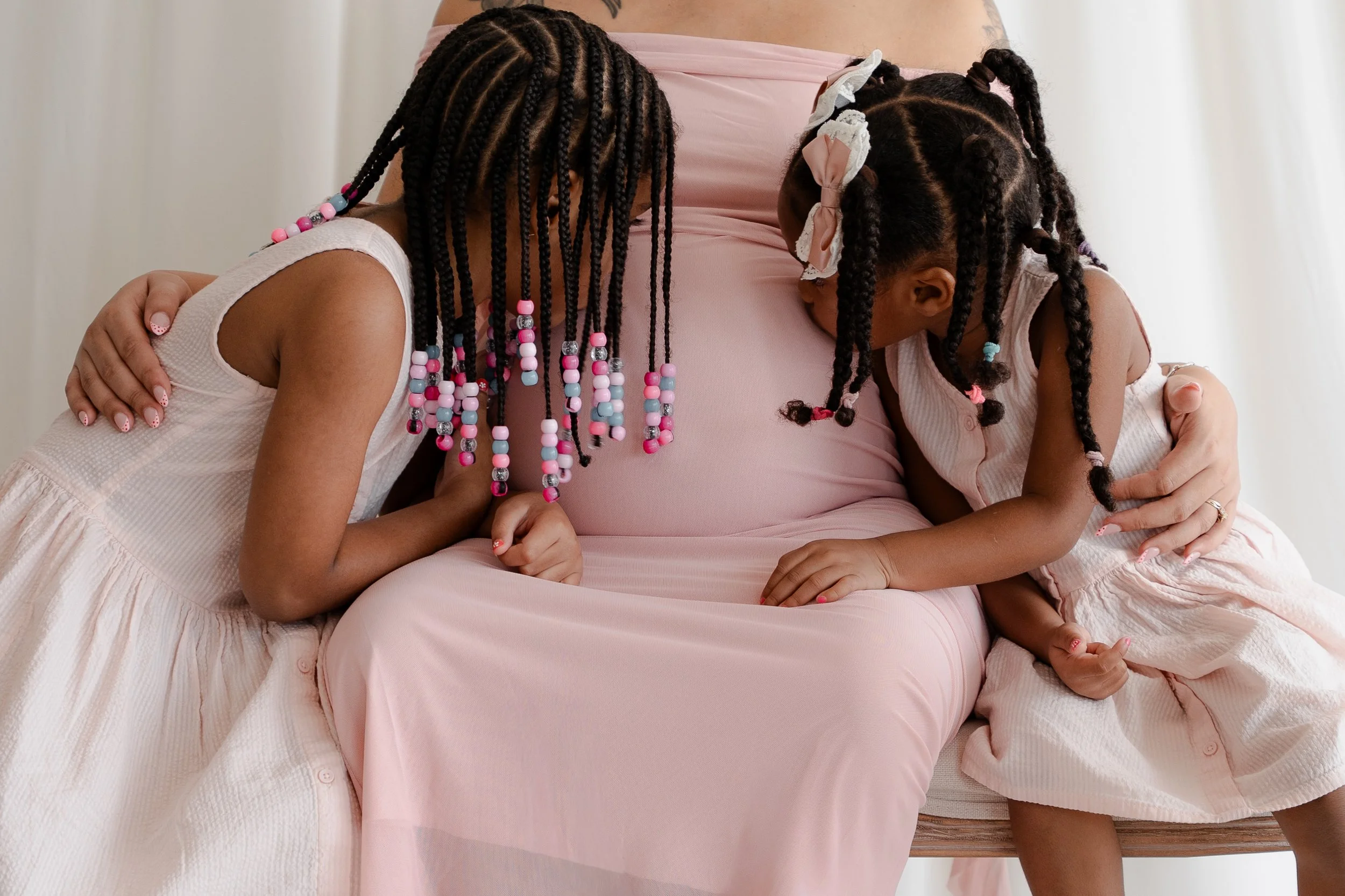 A woman and two young girls are hugging, with their heads bowed and eyes closed, in a tender moment.