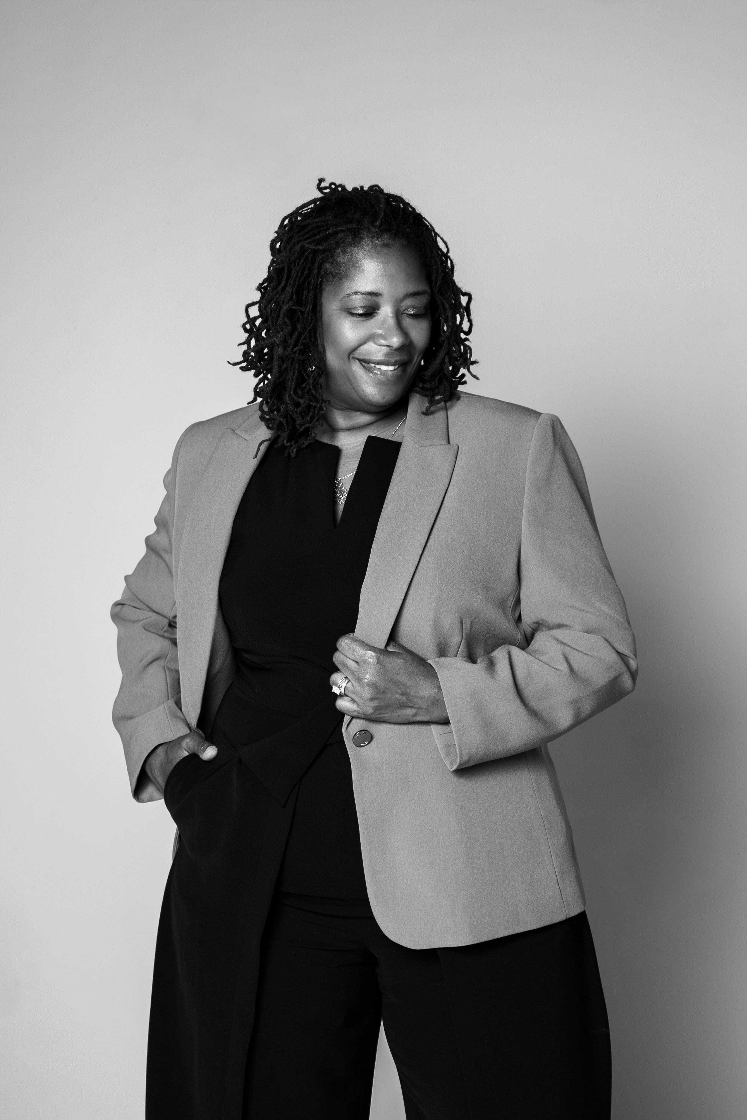 Black and white photo of an African American woman in a professional suit smiling and looking down, standing against a plain background.