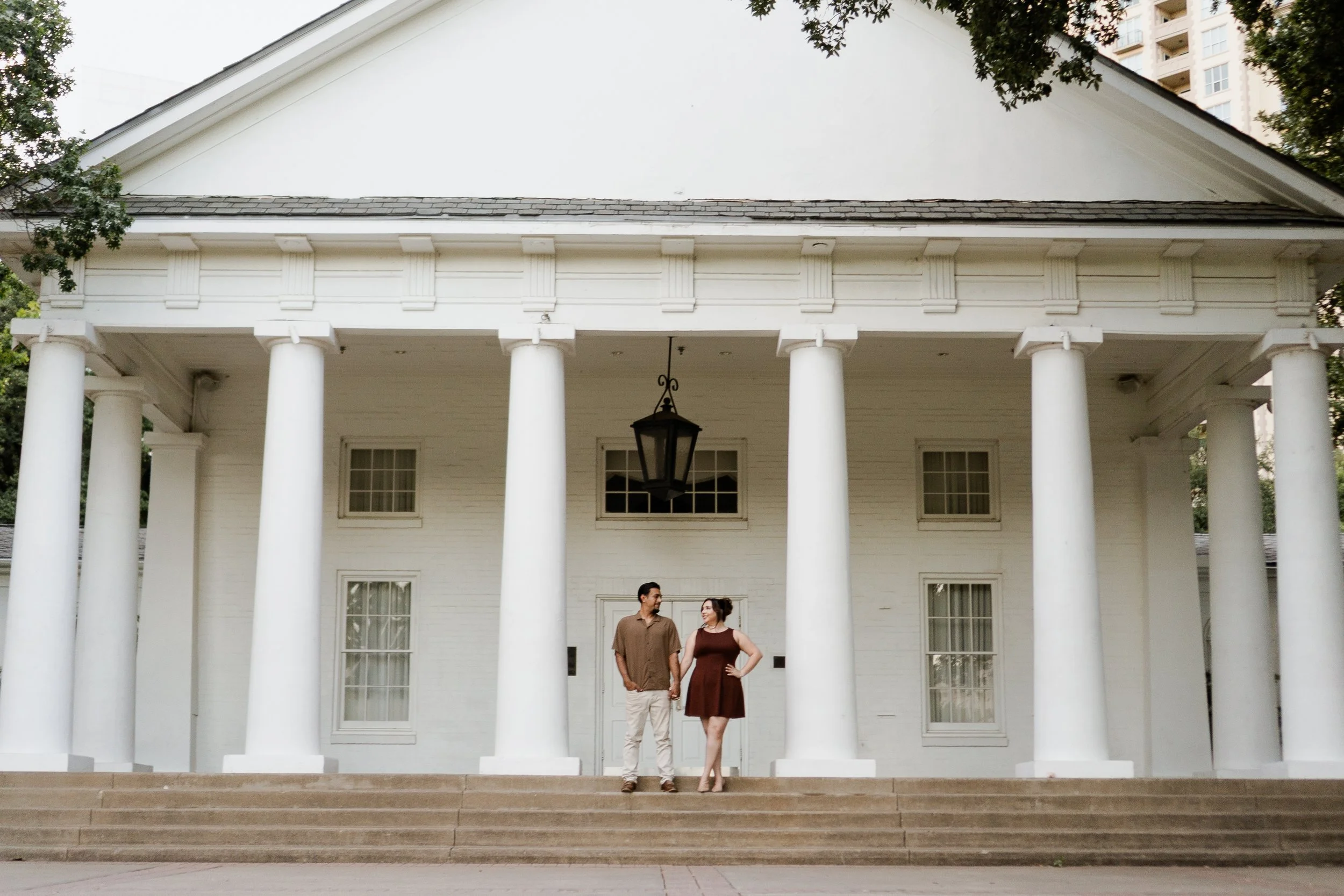 Couple standing on steps in front of a white building with large columns and a lantern hanging from its porch.