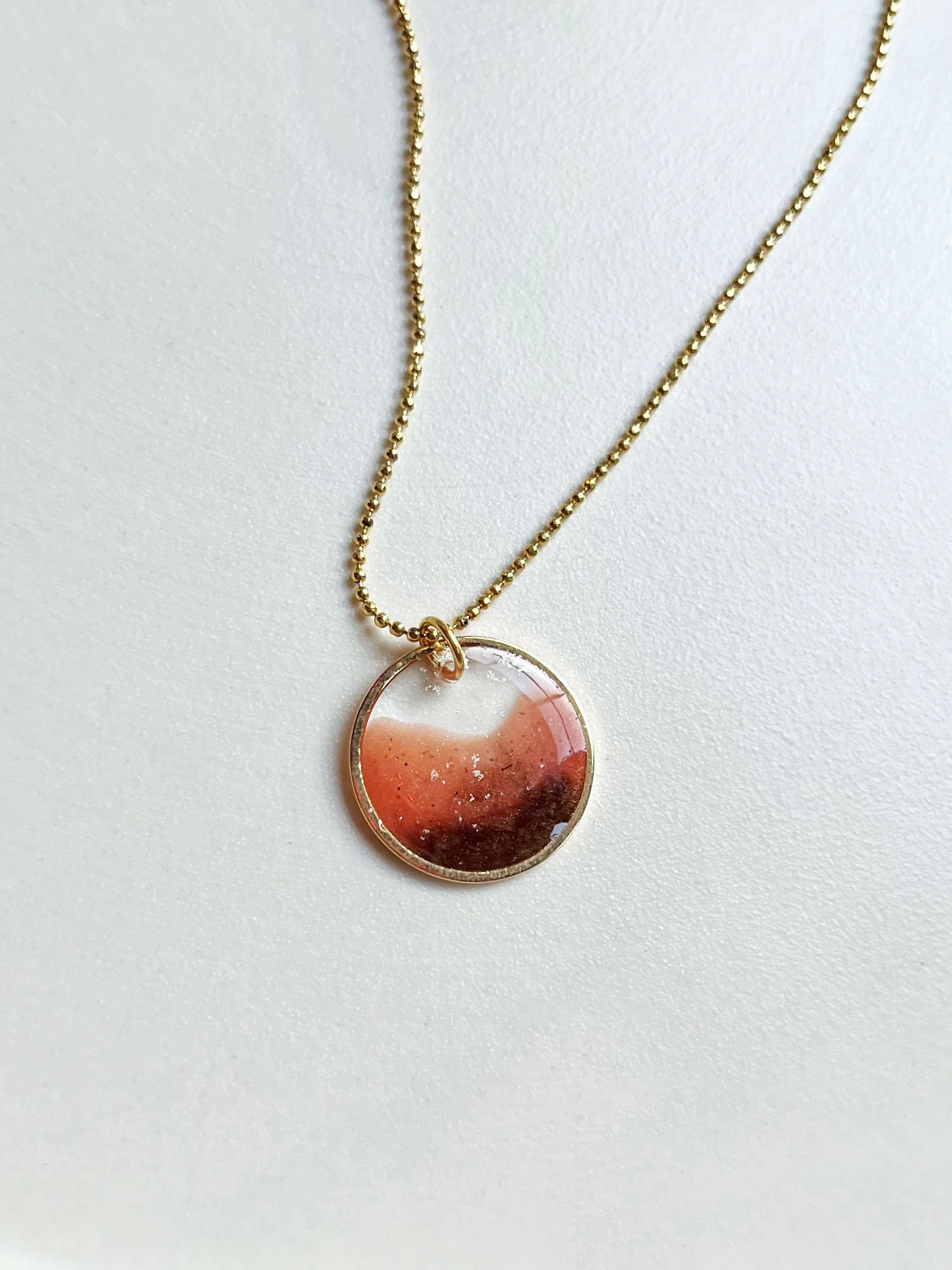 A gold and orange circular necklace with faceted bead chain