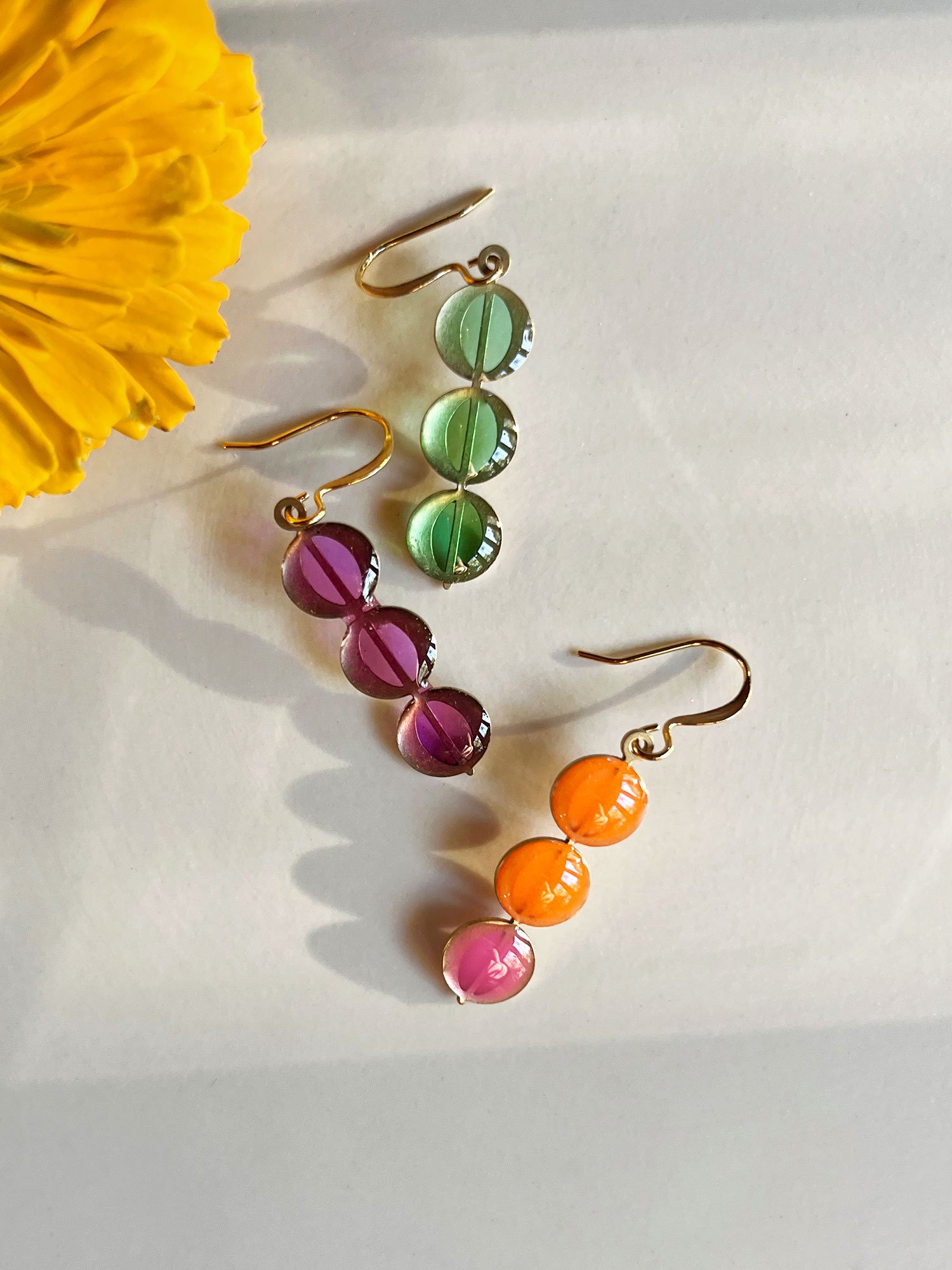 Three Juno Earrings variants in sunlight with yellow flower