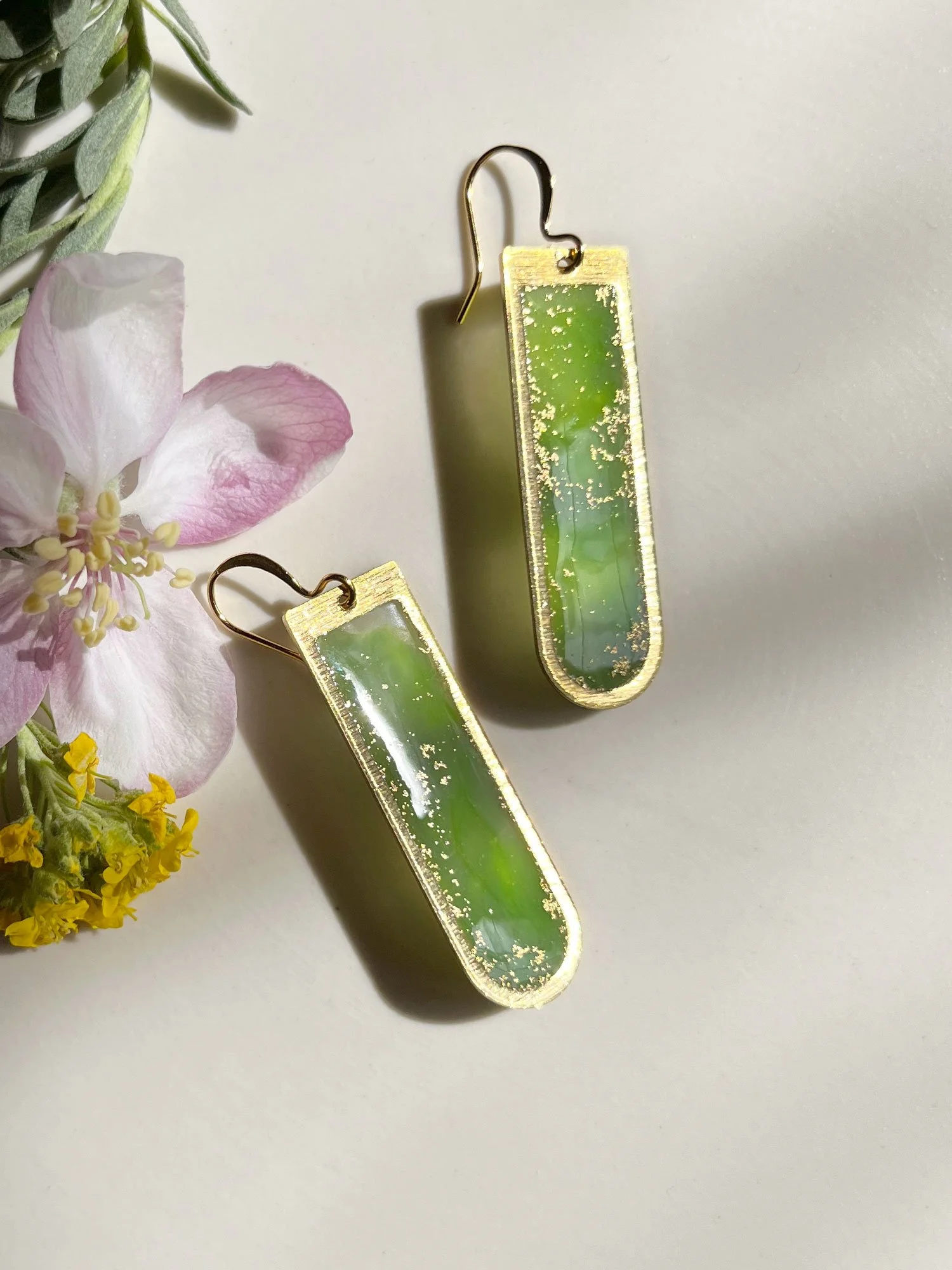 Long brass and resin earrings with swirling green resin filling.