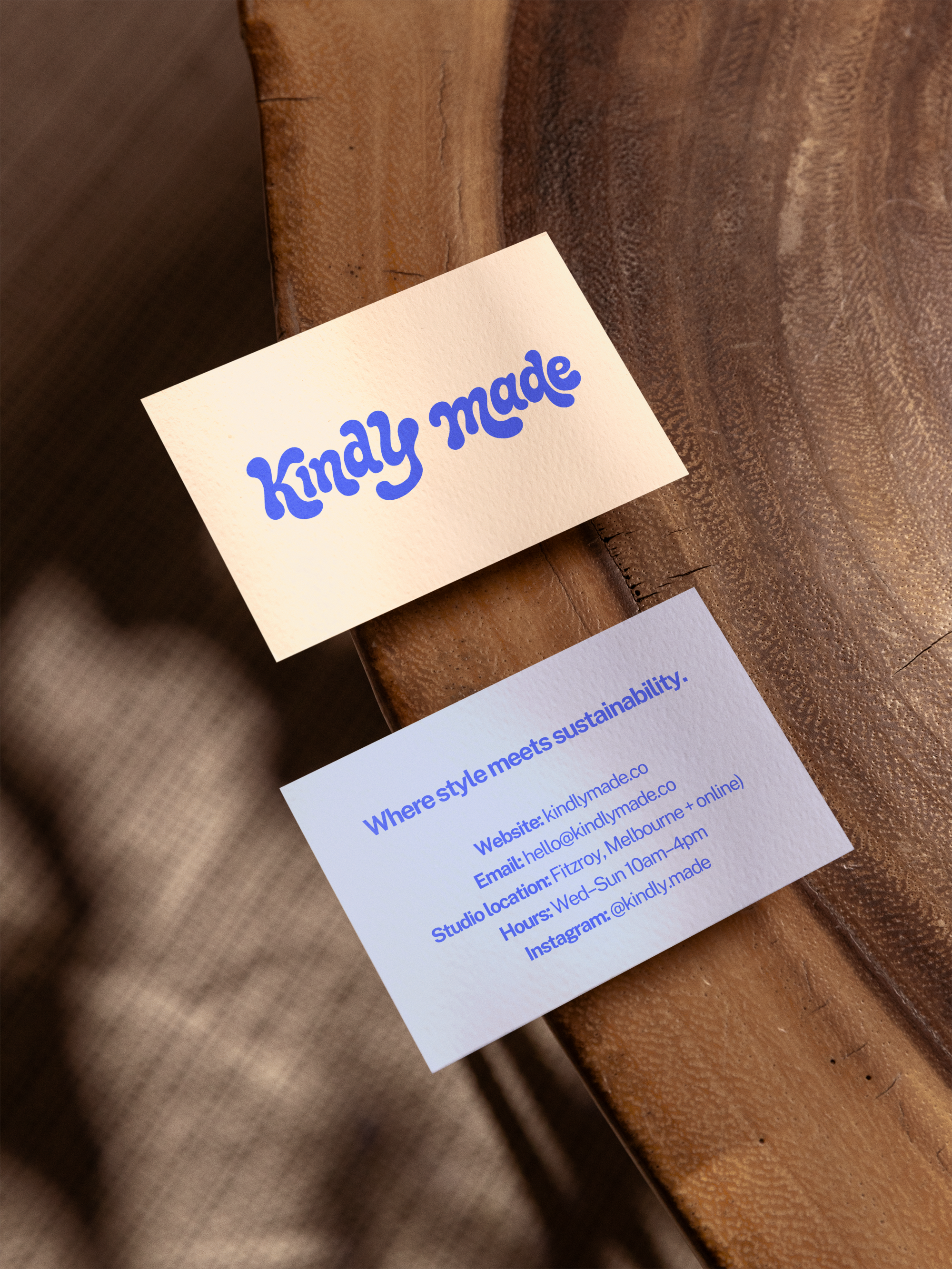 Close-up of a business card with the words 'kindly made' in blue, placed on a textured wooden surface.
