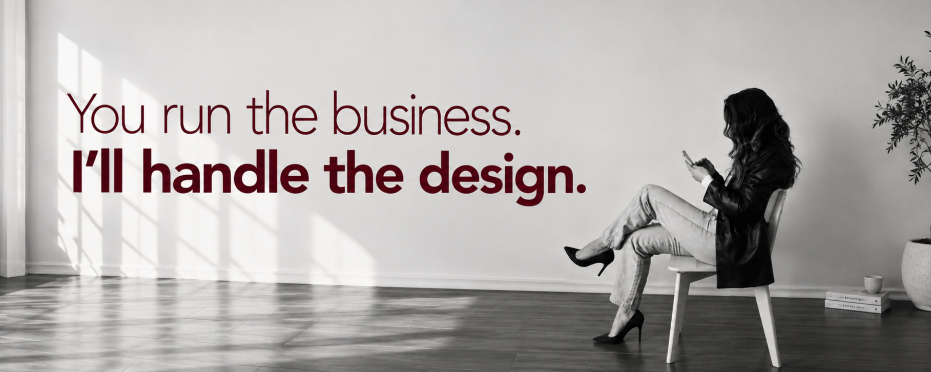 A woman sitting on a chair, looking at her phone in a modern, minimalistic room with a wooden floor, potted plant, and stacked books. Text on the wall reads, 'You run the business. I'll handle the design.'
