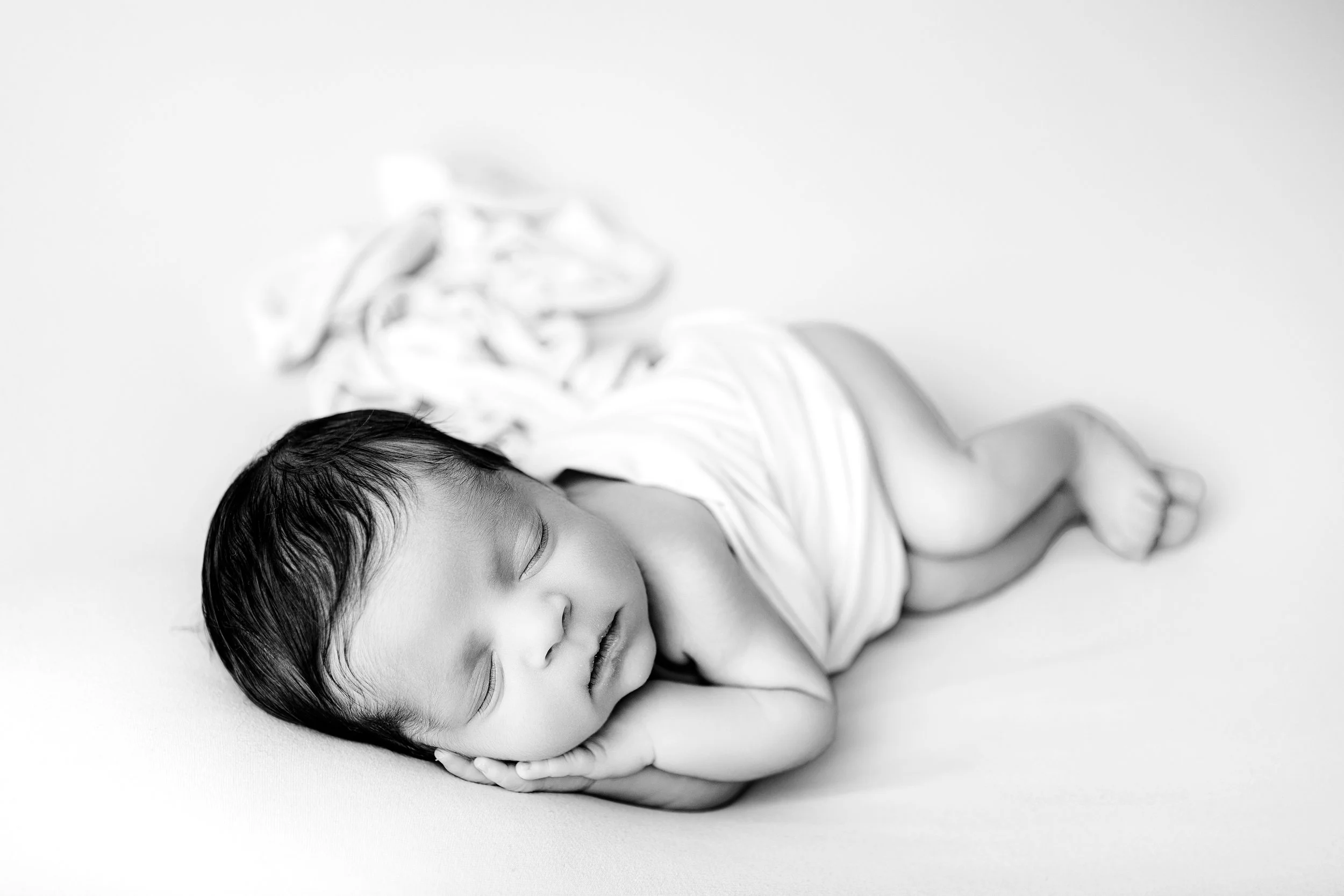 A sleeping young child with dark hair, lying on a soft surface with a peaceful expression, resting their head on their hand. baby boy Melbourne newborn photography South Morang