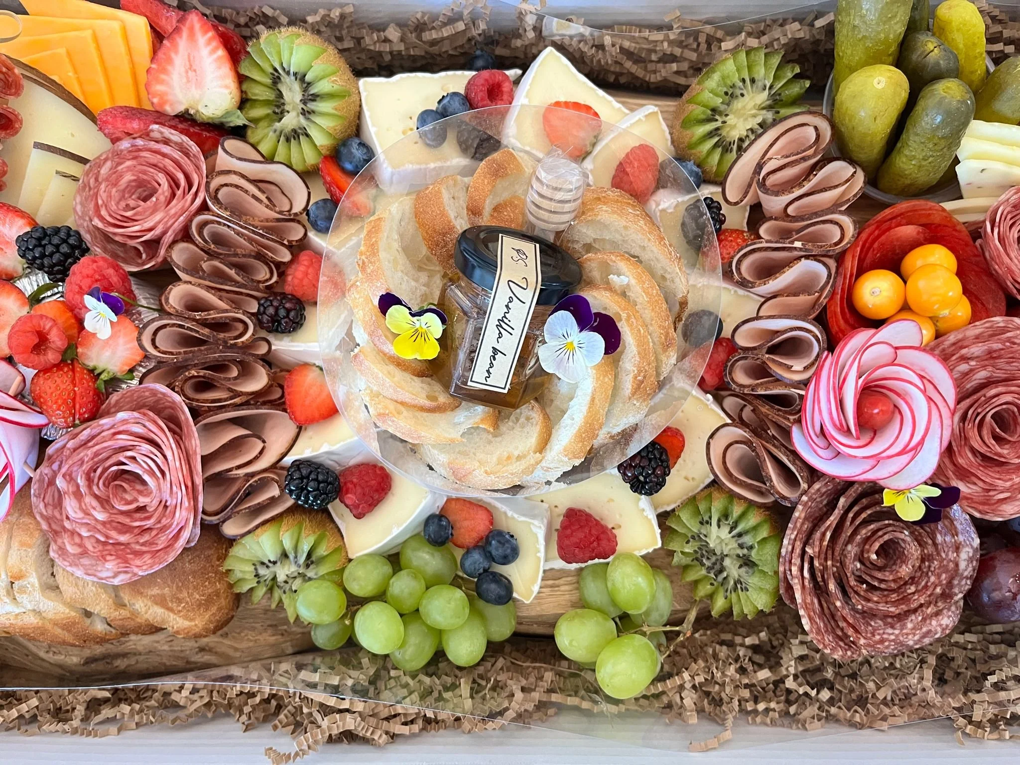 Assorted fruits, cheeses, and cured meats arranged as a decorative food platter, with roses and edible flowers for garnish.