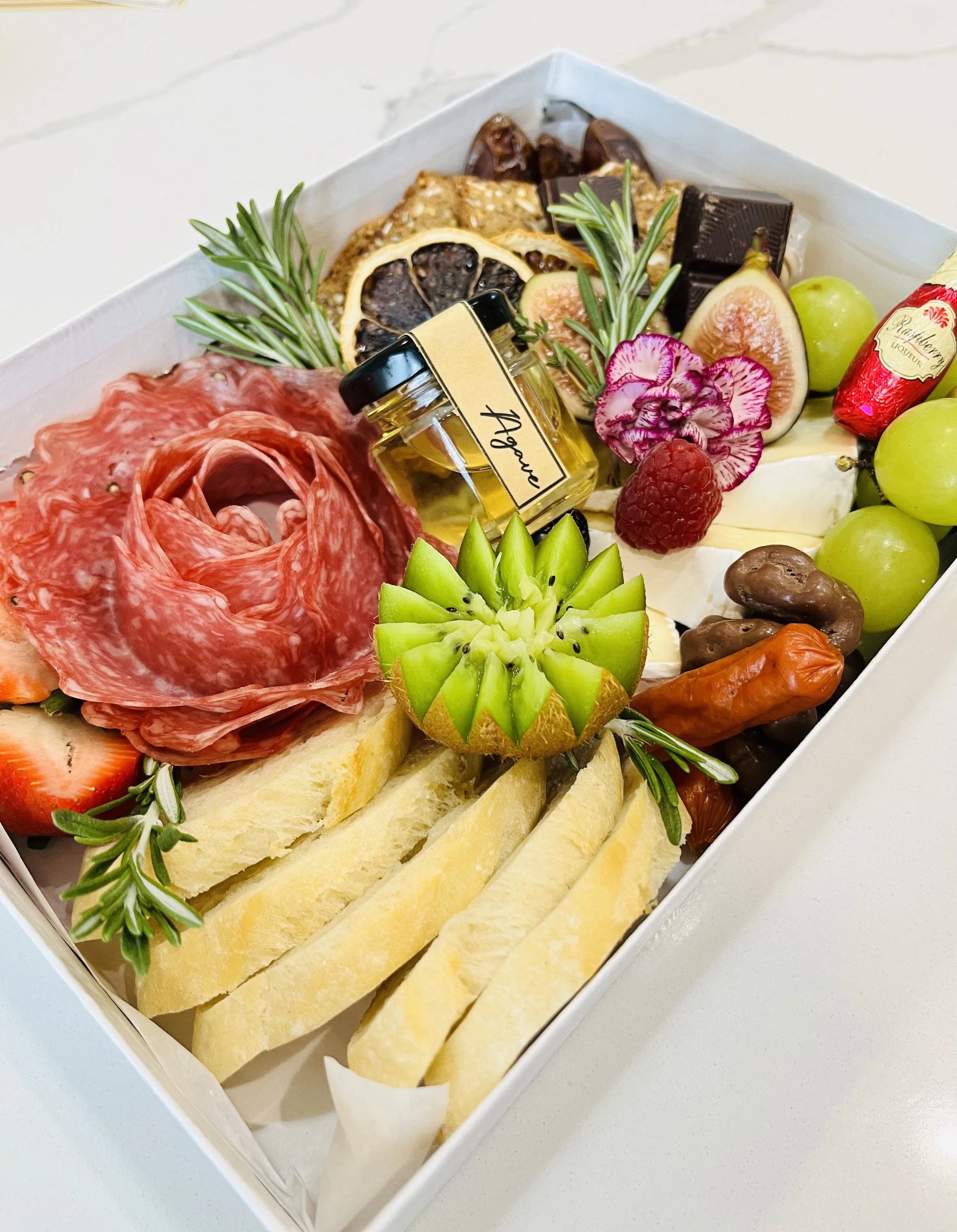 Charcuterie board with cured meats, cheeses, fresh fruits, herbs, and chocolates.