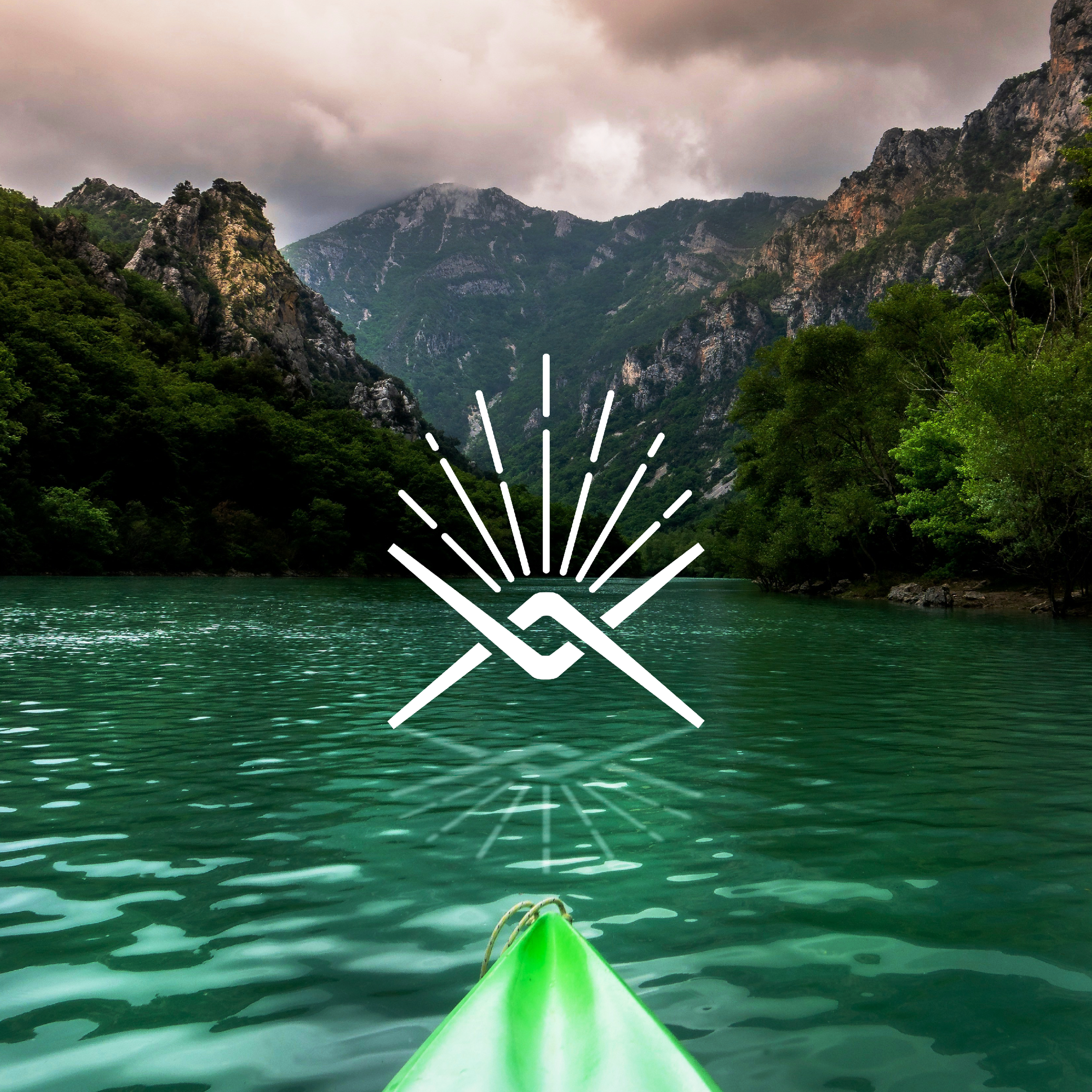 Photo of a green kayak in a lake surrounded by green forested mountains under cloudy sky.