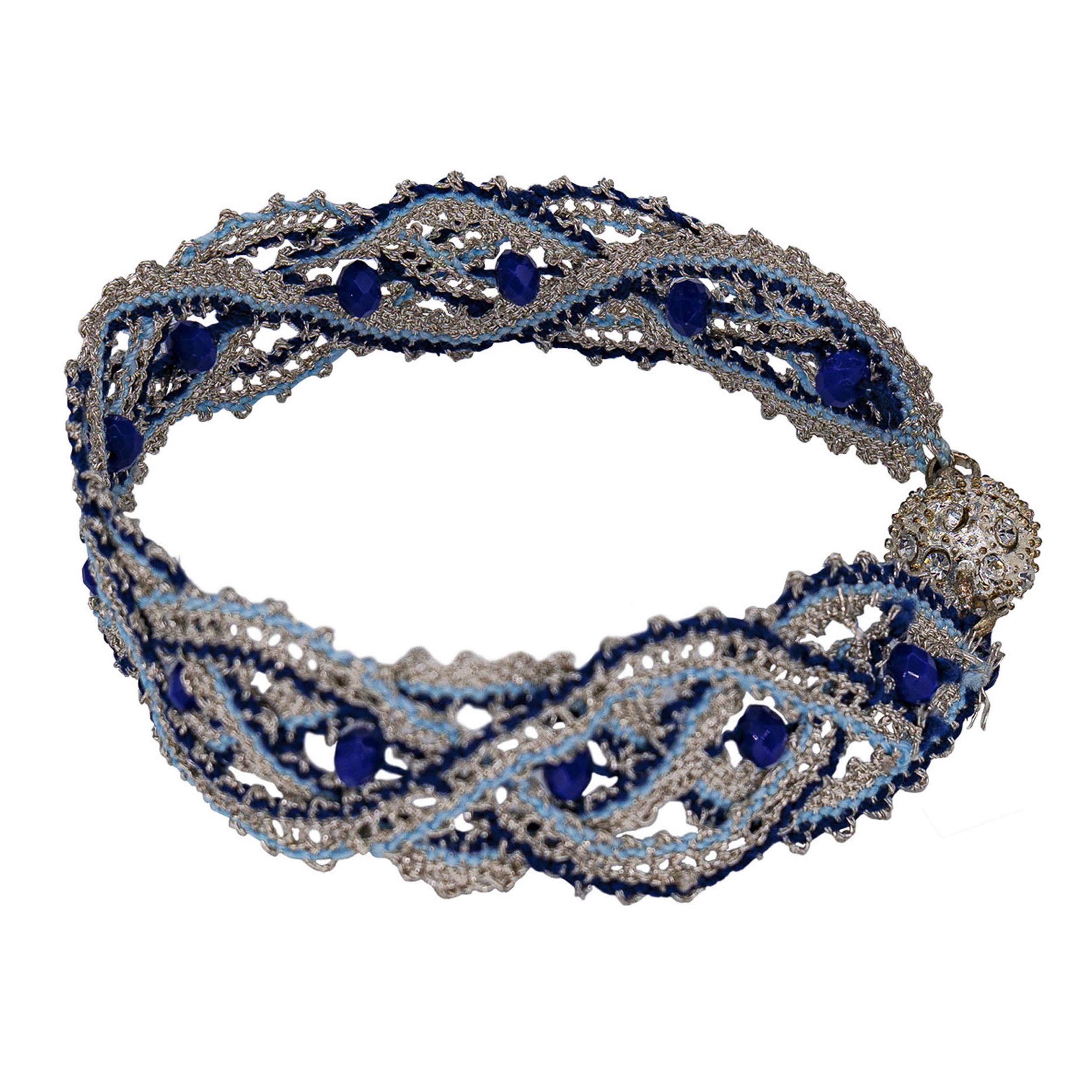 Bobbin lace wristband in silver with highligths in blue. Embellished with oval faceted glassbeads. Magnetic closure.