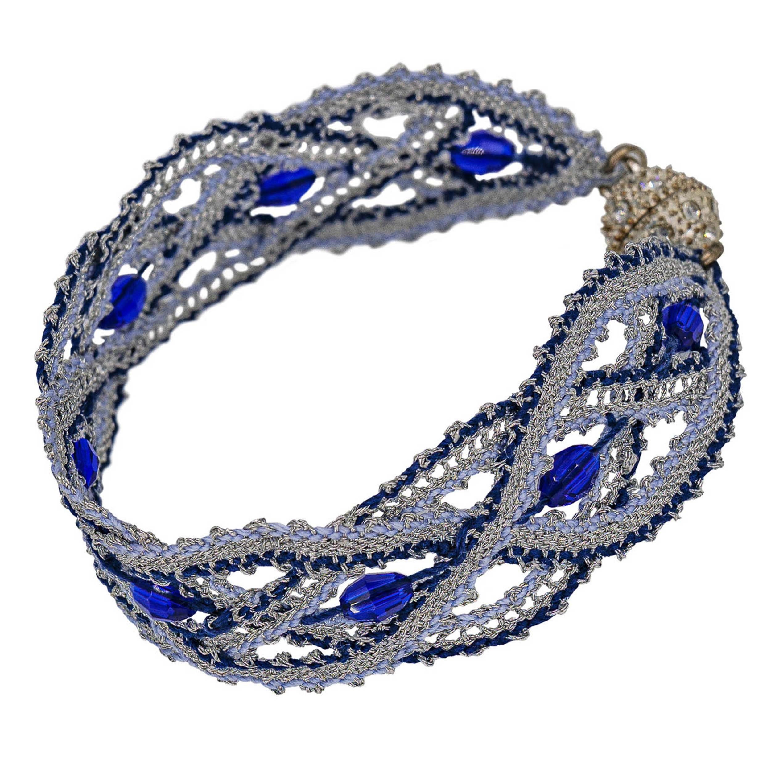 hand crafted bobbin lace wristband out of shimmery silver lurex thread combined with two blueish tones. Decorated with blue faceted glas beads and a beautiful magnet closure.
