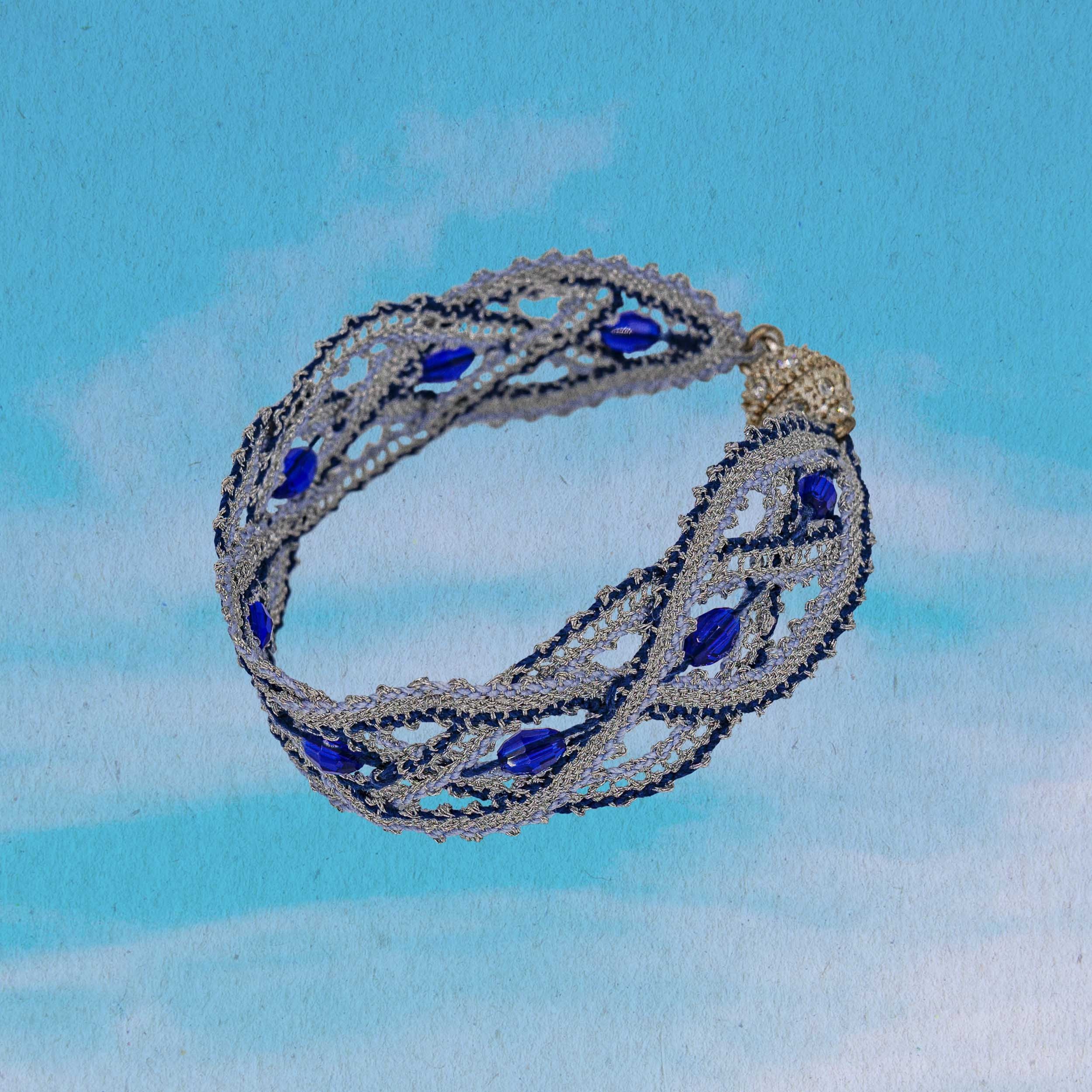 Old sicilian bobbin lace wristband with faceted glass beads and silver shining lurex thread infront of blue background