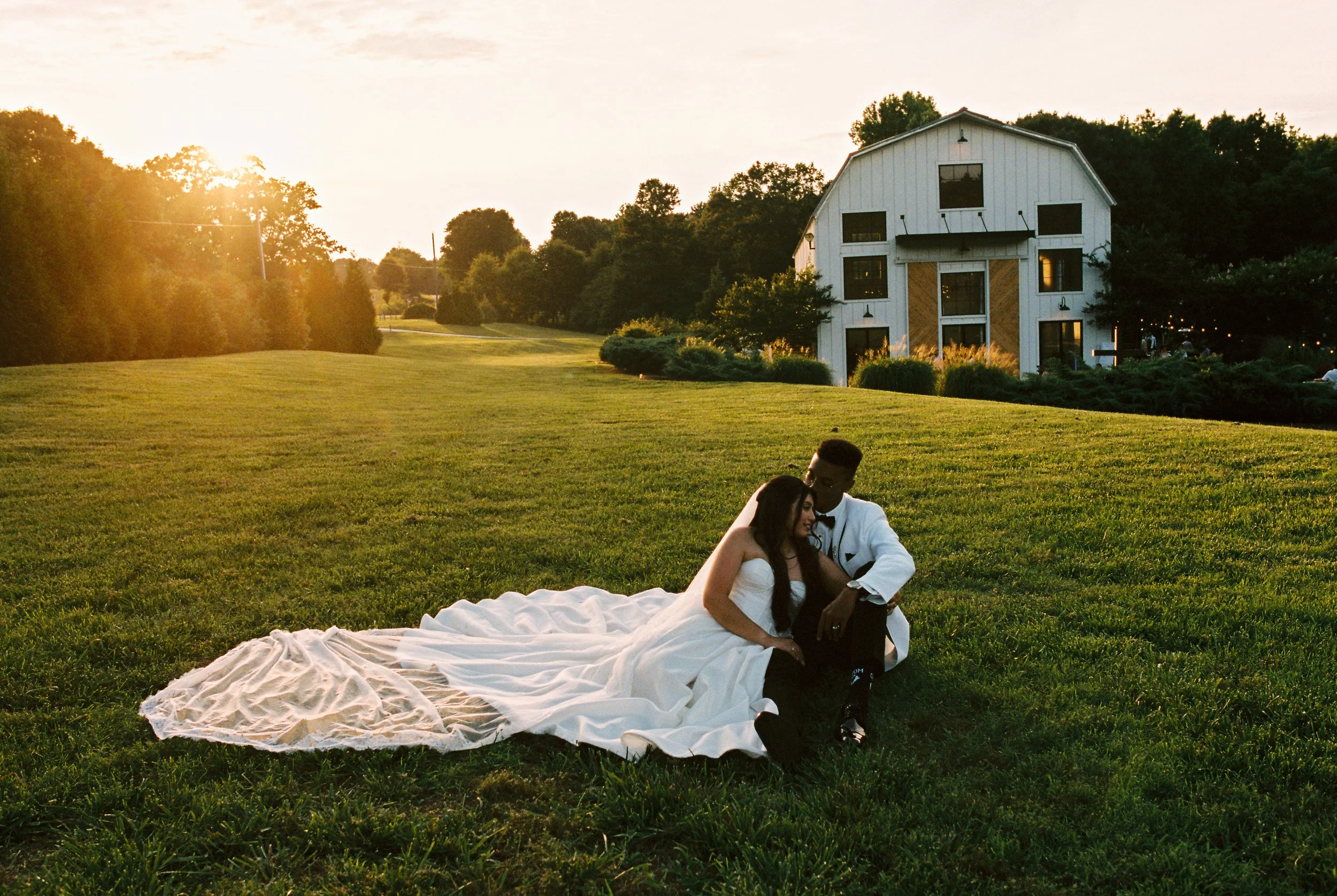 A couple sitting in the grass at sunset, the bride's train spread behind them