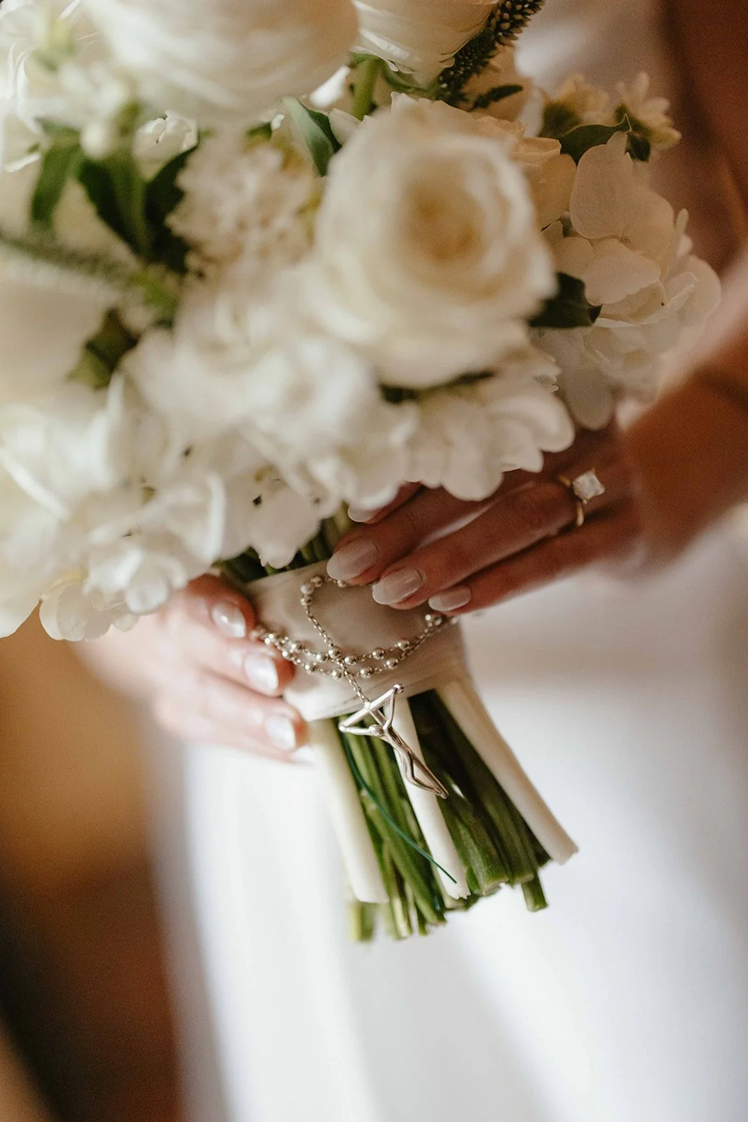 Close-up of a bride holding a bouquet of white flowers, with a silver necklace featuring a star-shaped pendant resting on her hands.