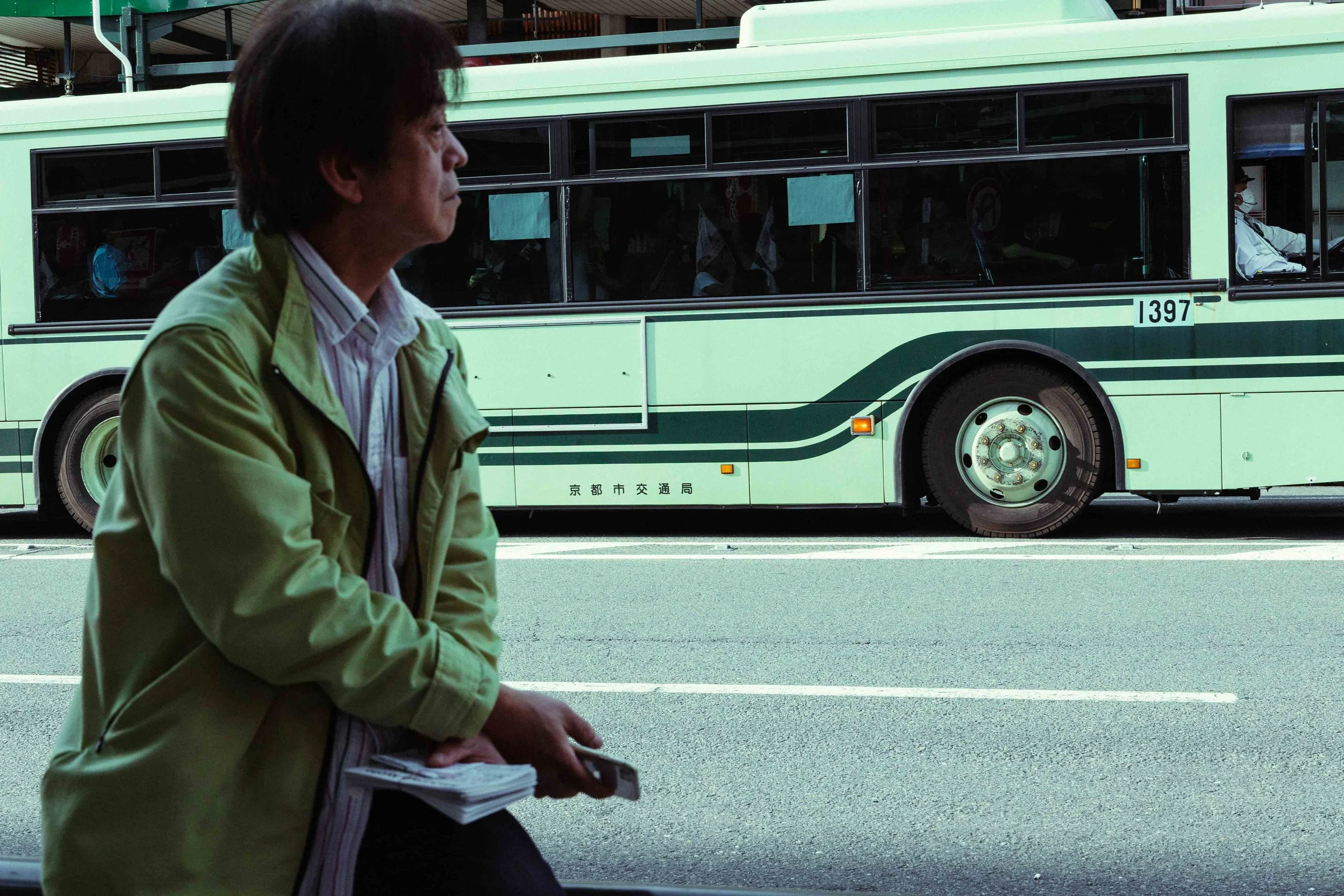 A man is looking ad the main street of Kyoto and in the background a bus is going by