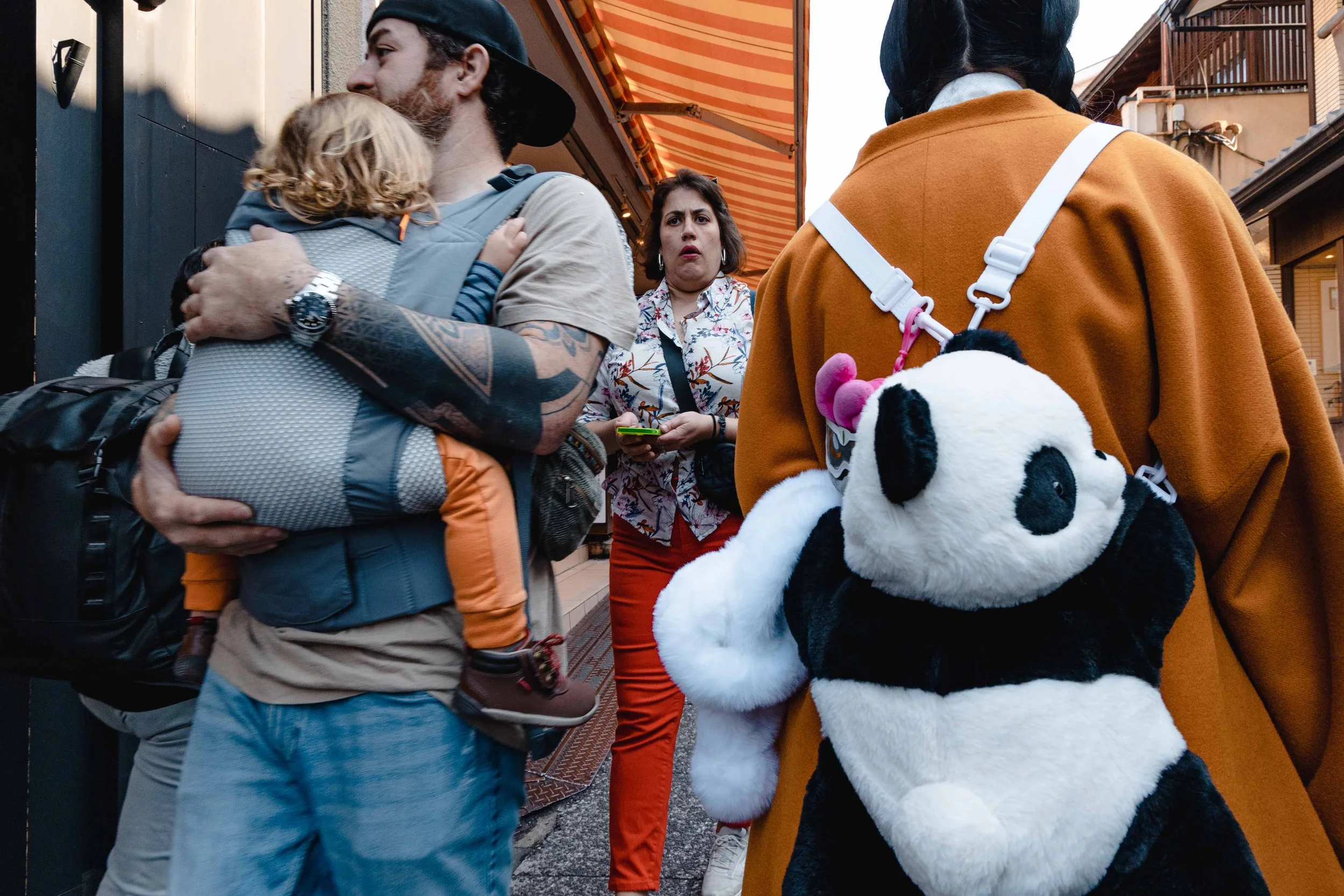 street of Kyoto full of tourists with detail of a dad holding his kid and next to them a woman with a panda backpack