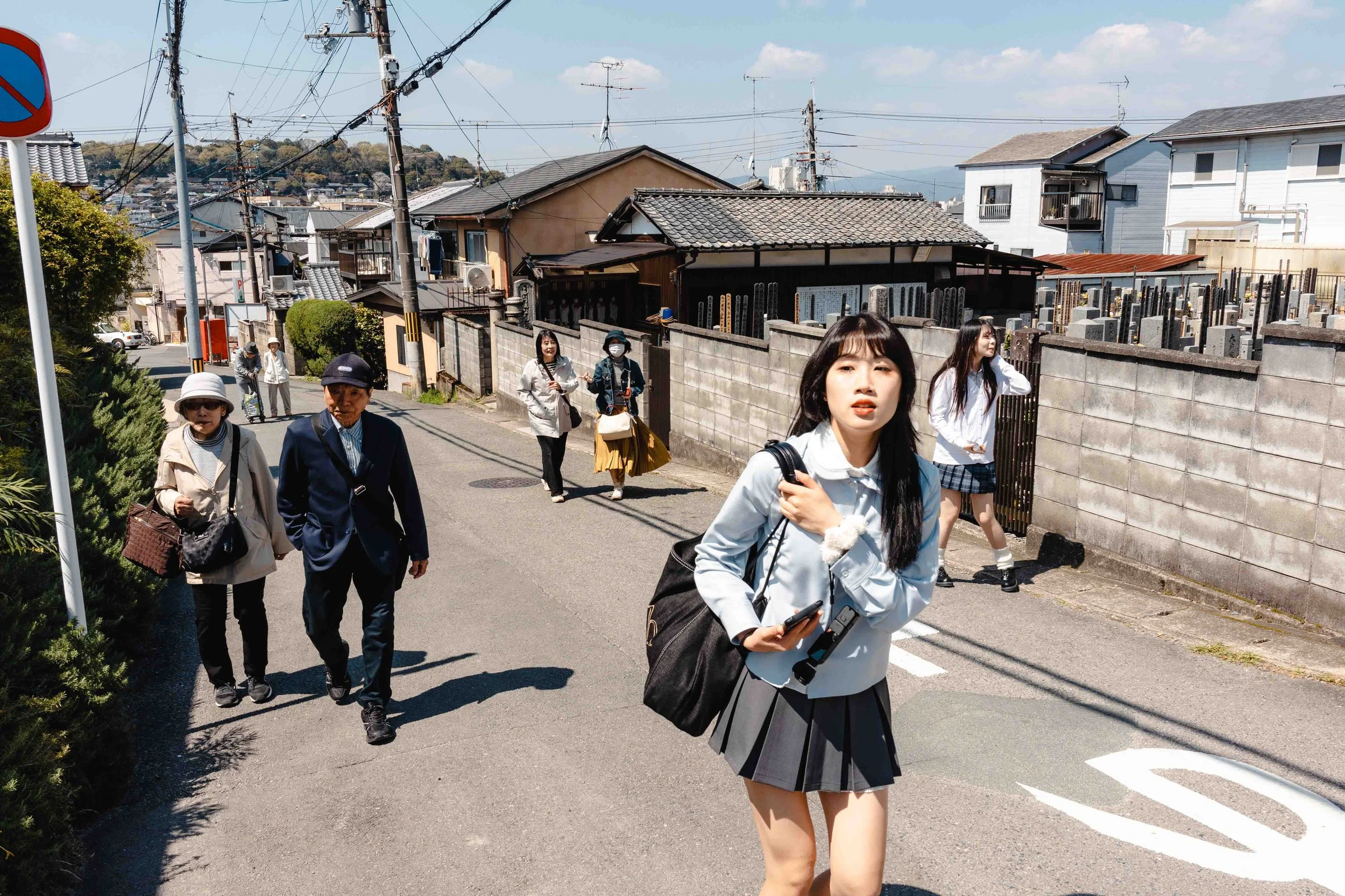 Japanese people walk in a street in Kyoto. In the background some old houses and a cemetery