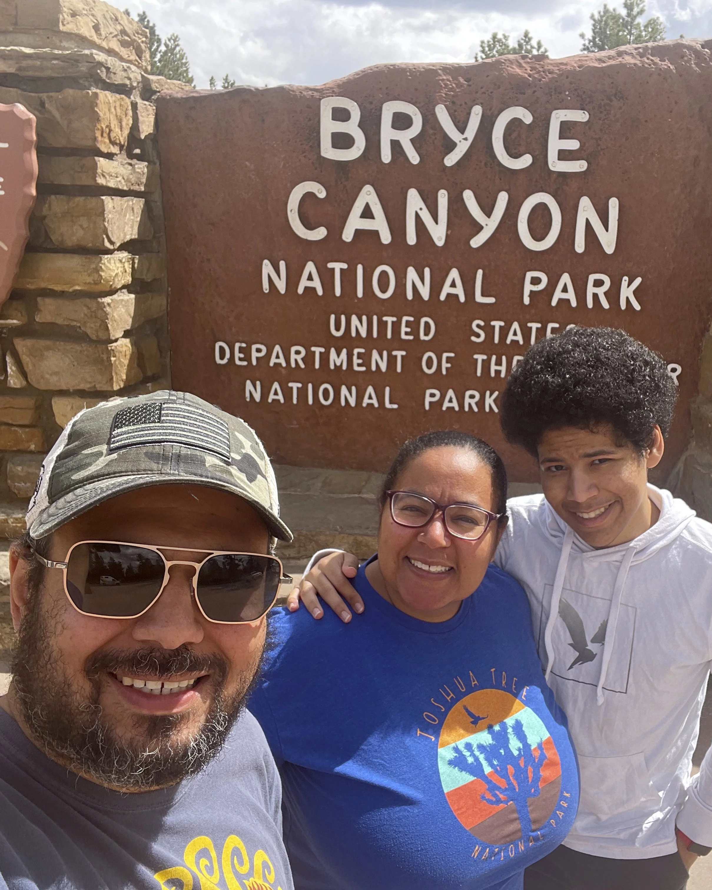 Edwin, Jessely and EJ Soto standing in front of the Bryce Canyon National Park sign as a family.