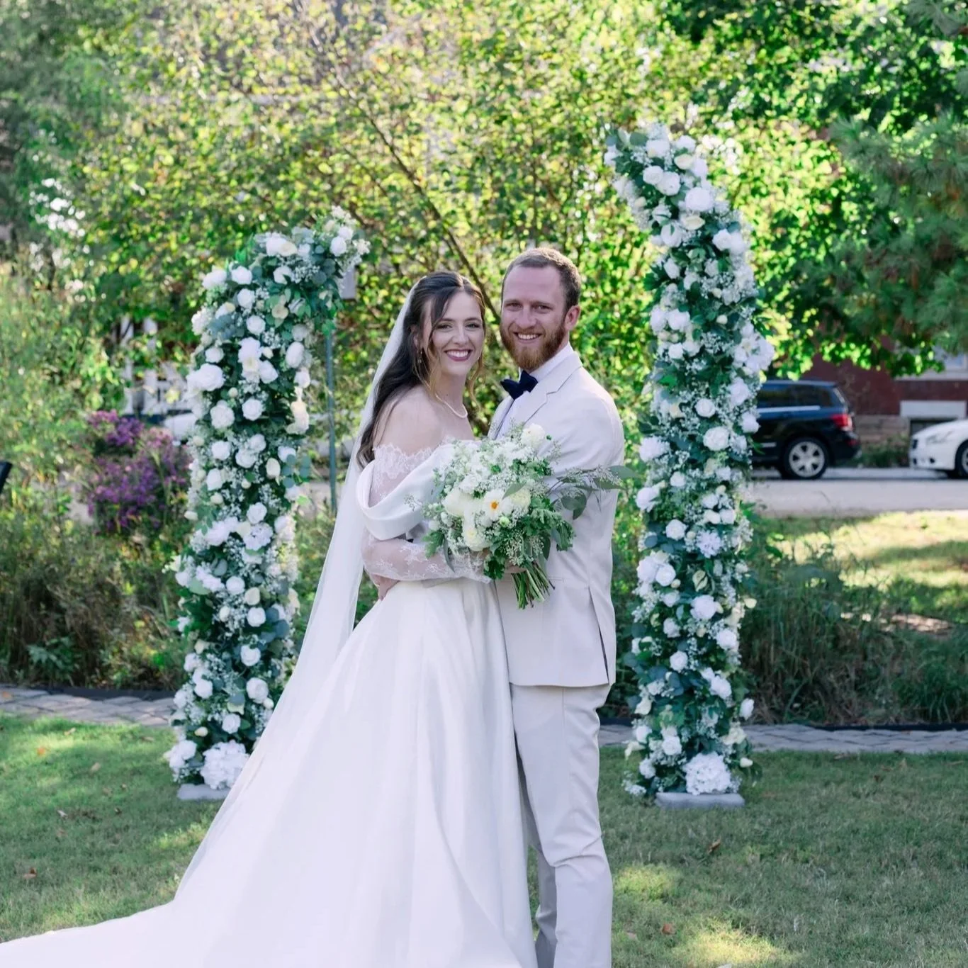 bride and groom at outdoor ceremony with greenery and white floral horn arch