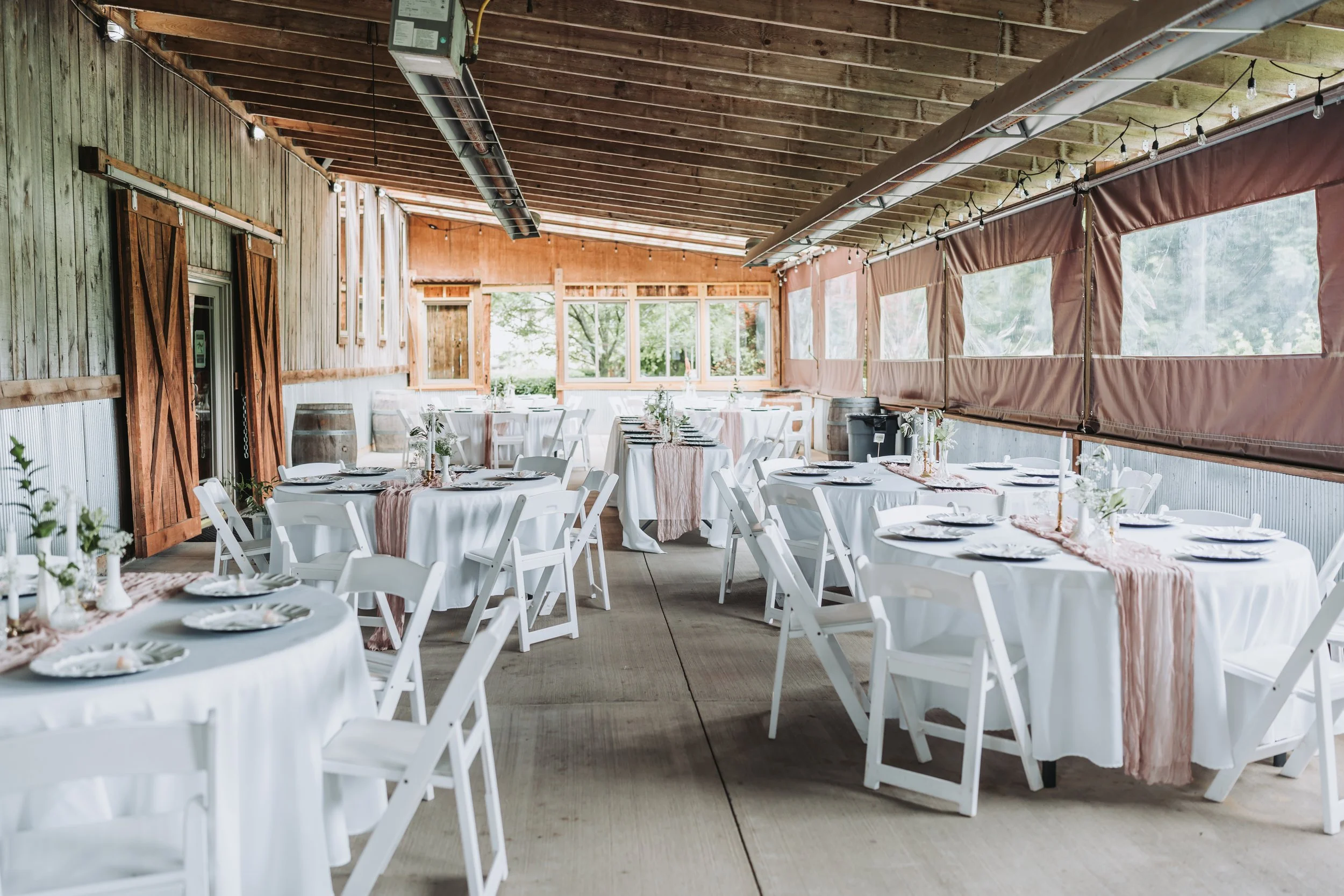 guest tables at a barn wedding venue with white tablecloths overlaid with dusty pink cheesecloth and centerpieces of bud vases and brass candlesticks
